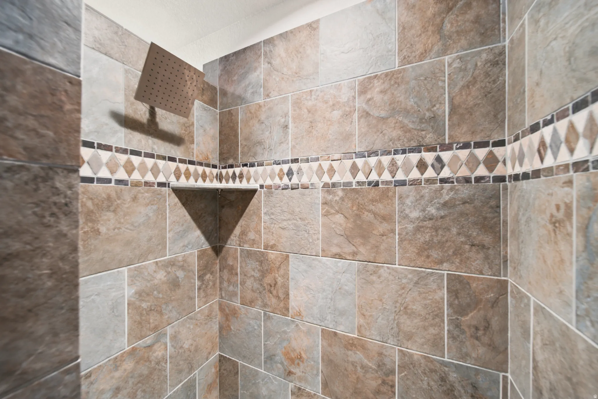 Shower enclosure featuring large format stone-look tiles, a mosaic accent band, a rain showerhead, and a built-in corner shelf