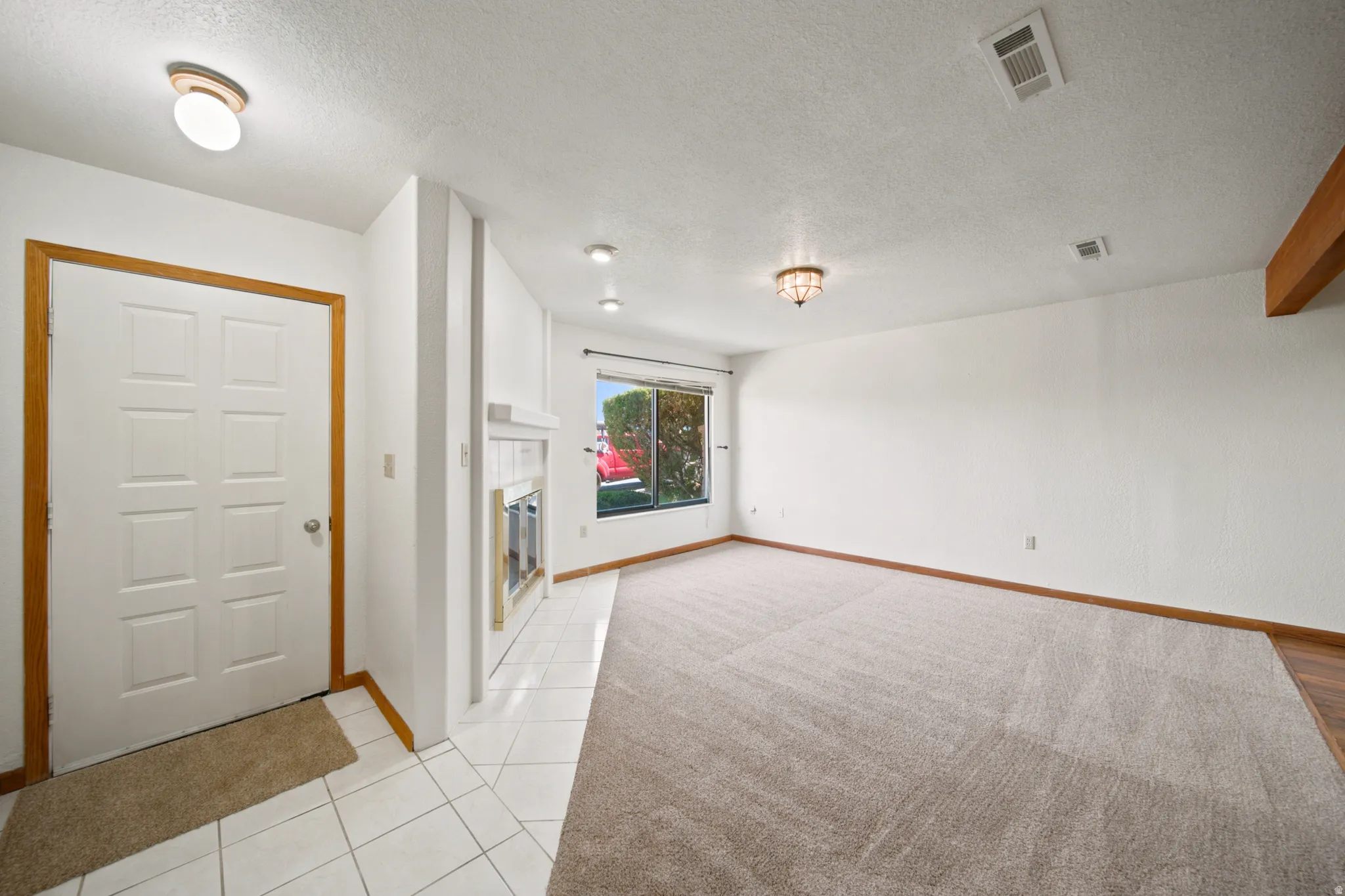 Bright living area featuring a white paneled entry door, tiled entryway, white fireplace with hearth, recessed lighting, and a large window