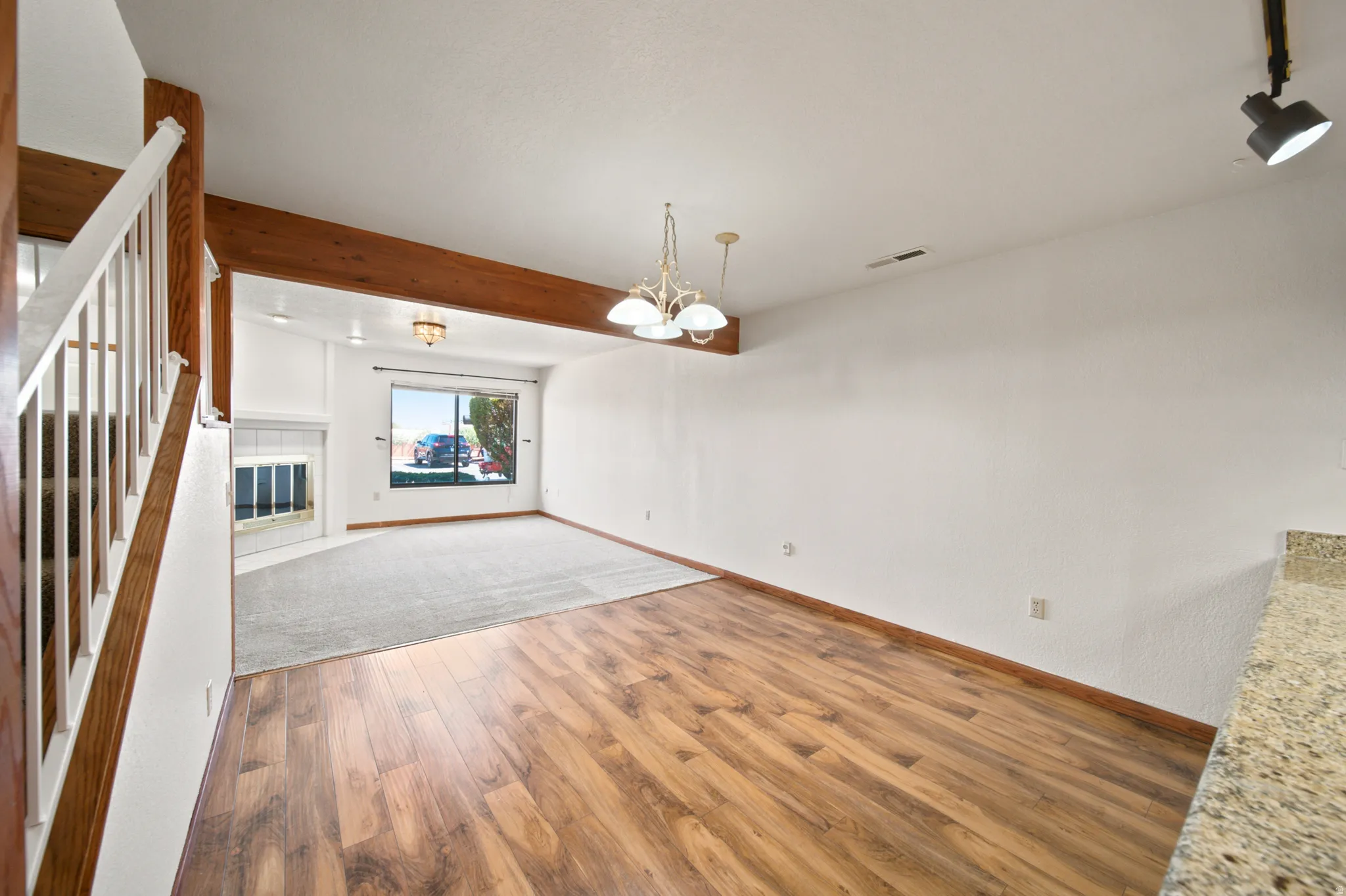 Living area featuring wood-finish flooring, a carpeted section, and a fireplace with a white mantel