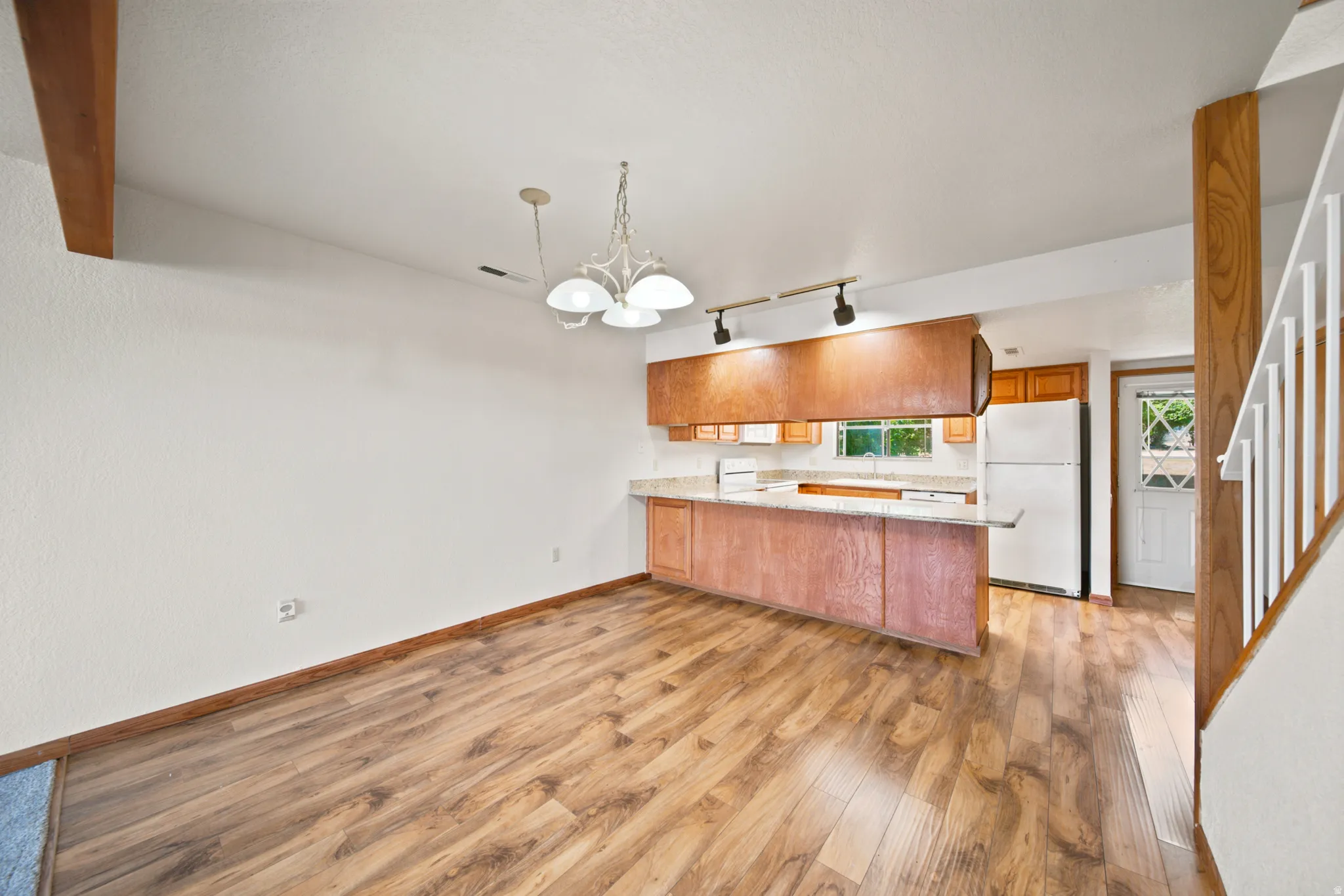 Open-concept room featuring wood-finish flooring, white walls, and a recessed kitchen area