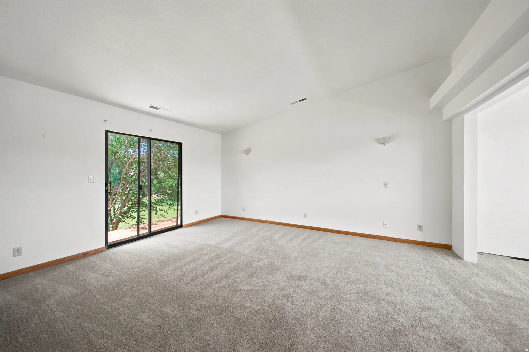 Spacious room featuring light gray carpet flooring, white walls, and a prominent sliding glass door