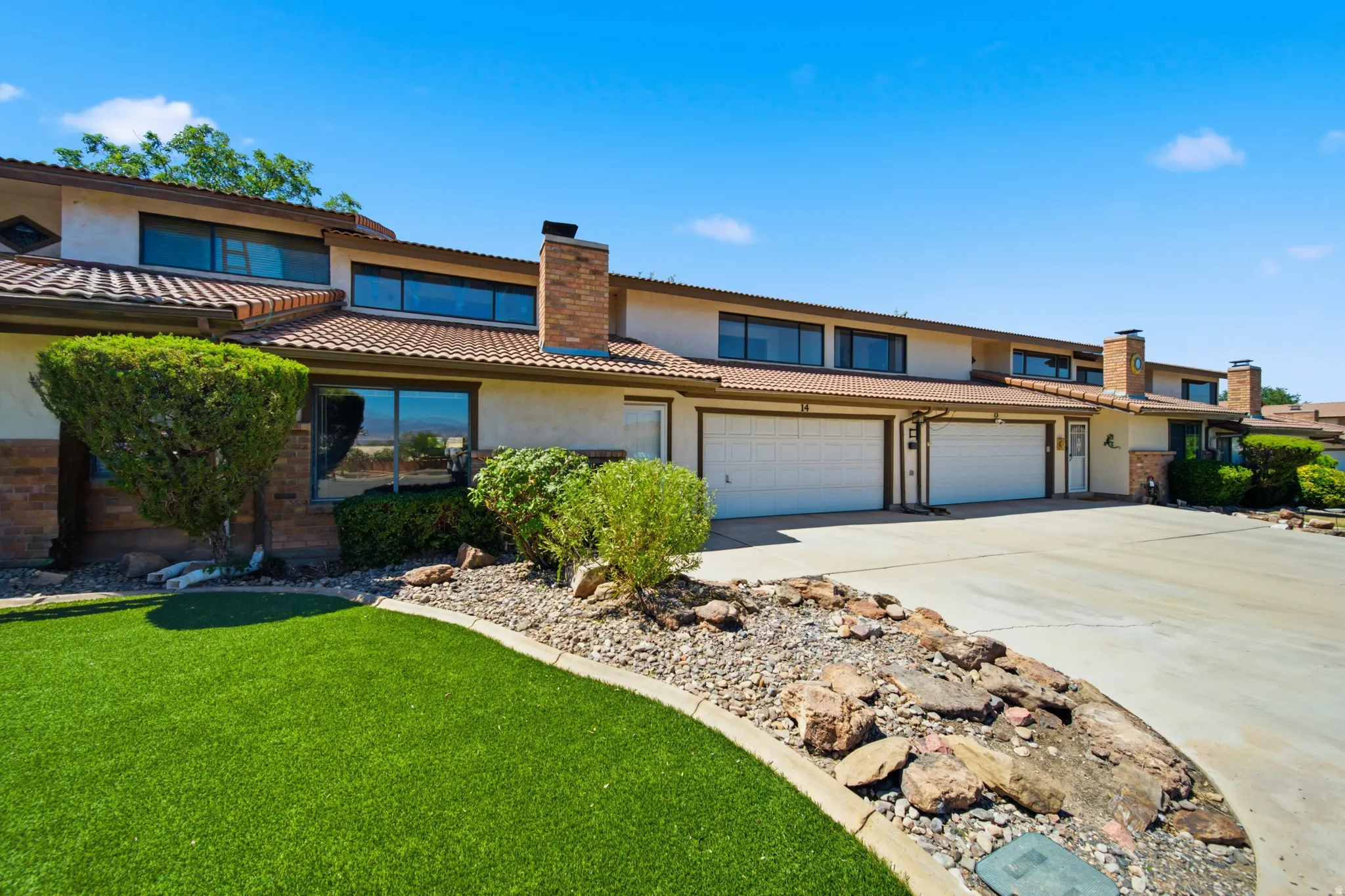Front exterior featuring a terracotta tile roof, stucco finish, brick accents, multiple windows, and a two-car garage