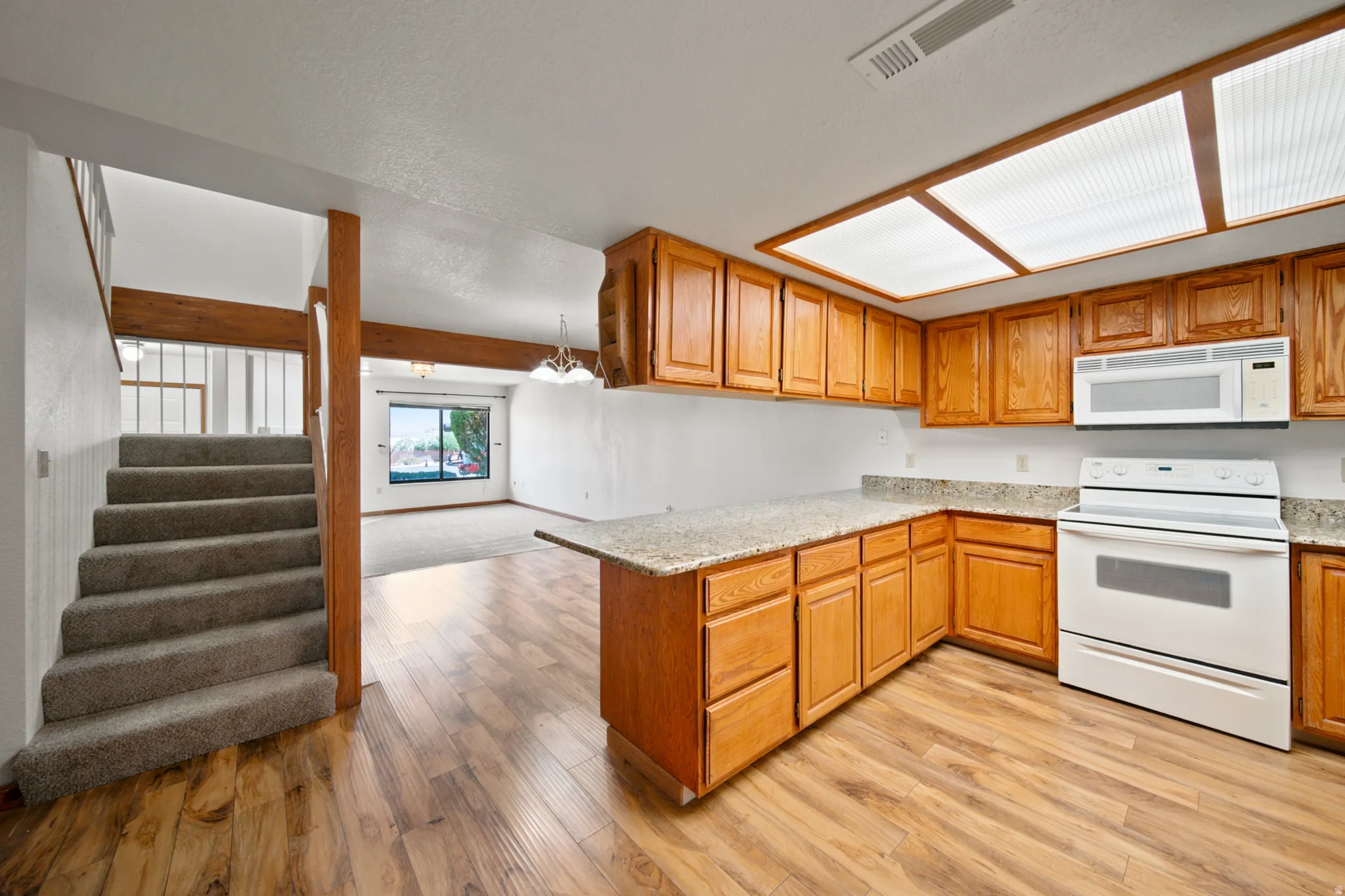 Kitchen with wood-finish flooring, light wood cabinetry, white appliances, and a light-colored countertop