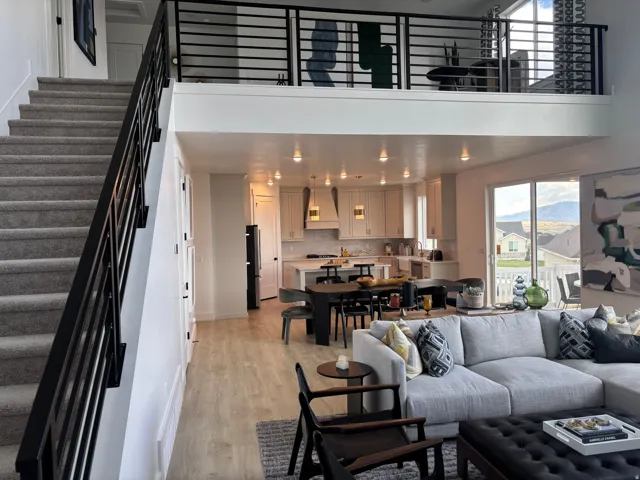 Open-concept living space featuring a modern black metal railing staircase, a kitchen with light cabinetry and an island, wood-finish flooring, and sliding glass doors leading to an outdoor space