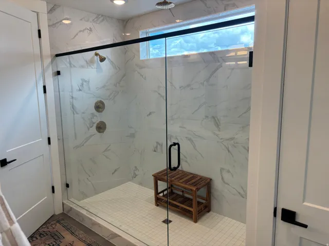 Spacious shower enclosure featuring a frameless glass door with matte black hardware, white subway tile flooring, and large format wall tiles with a subtle veining pattern