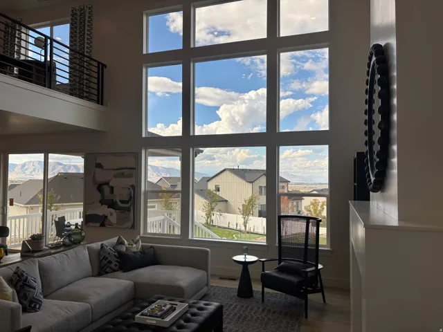 Two-story living area featuring extensive window walls, a Juliet balcony with black metal railing, and light wood-finish flooring