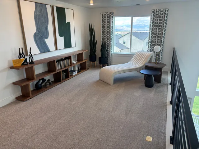 Spacious loft area featuring a large window, neutral carpet, and a built-in wood-finish shelving unit