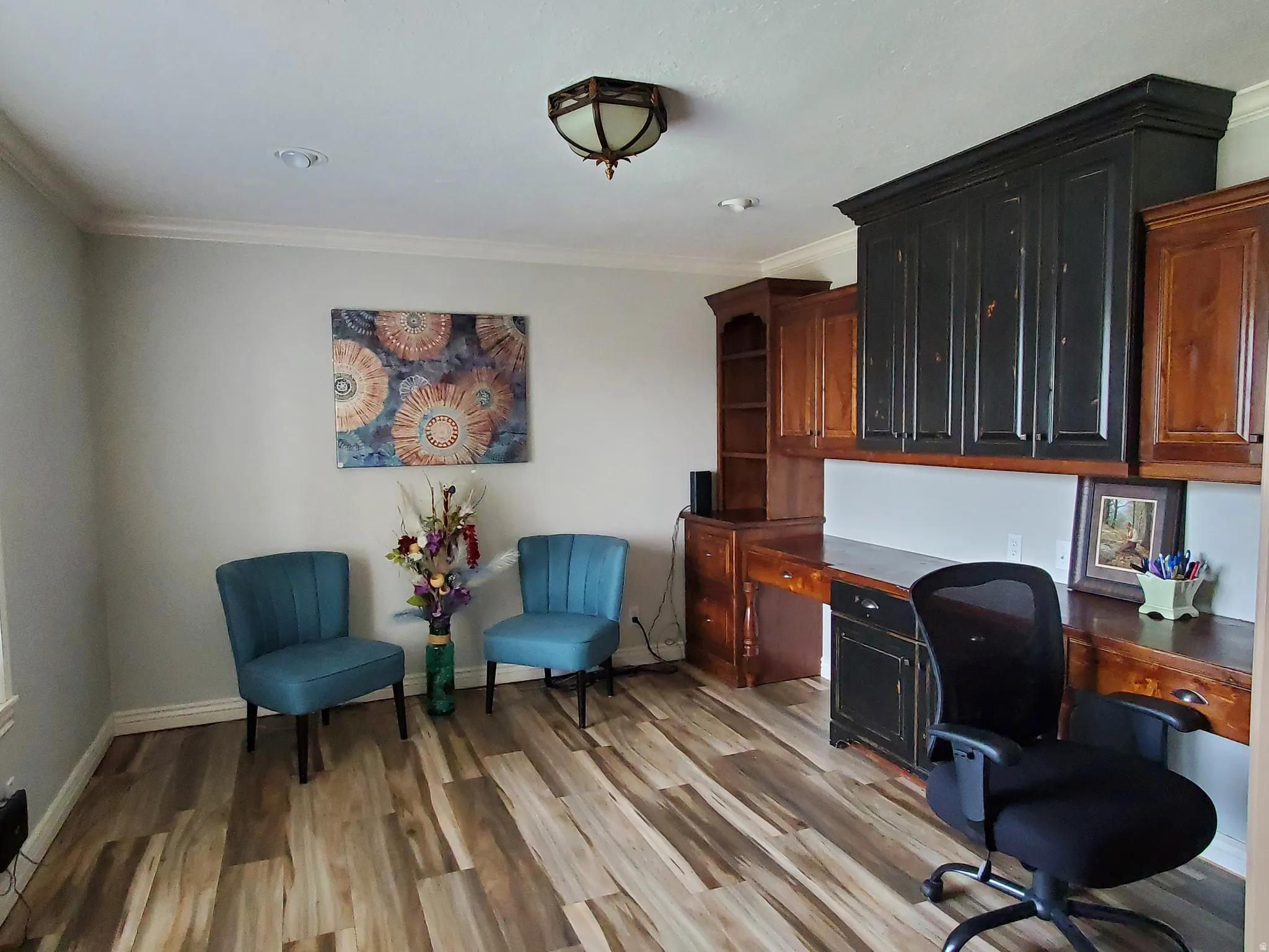 Dedicated office space featuring extensive built-in cabinetry, wood-finish flooring, and crown molding