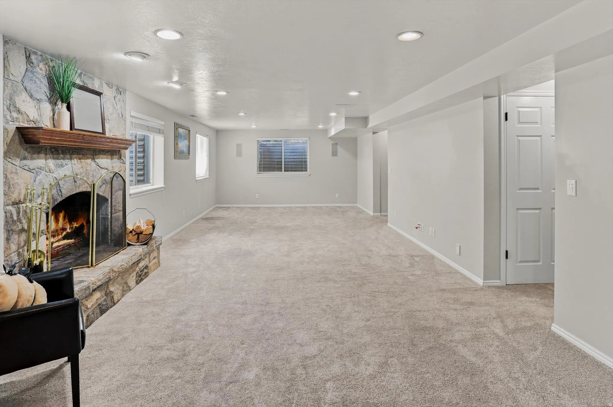 Spacious room featuring a stone-clad fireplace with a wood mantel, soft carpet flooring, recessed lighting, and multiple windows