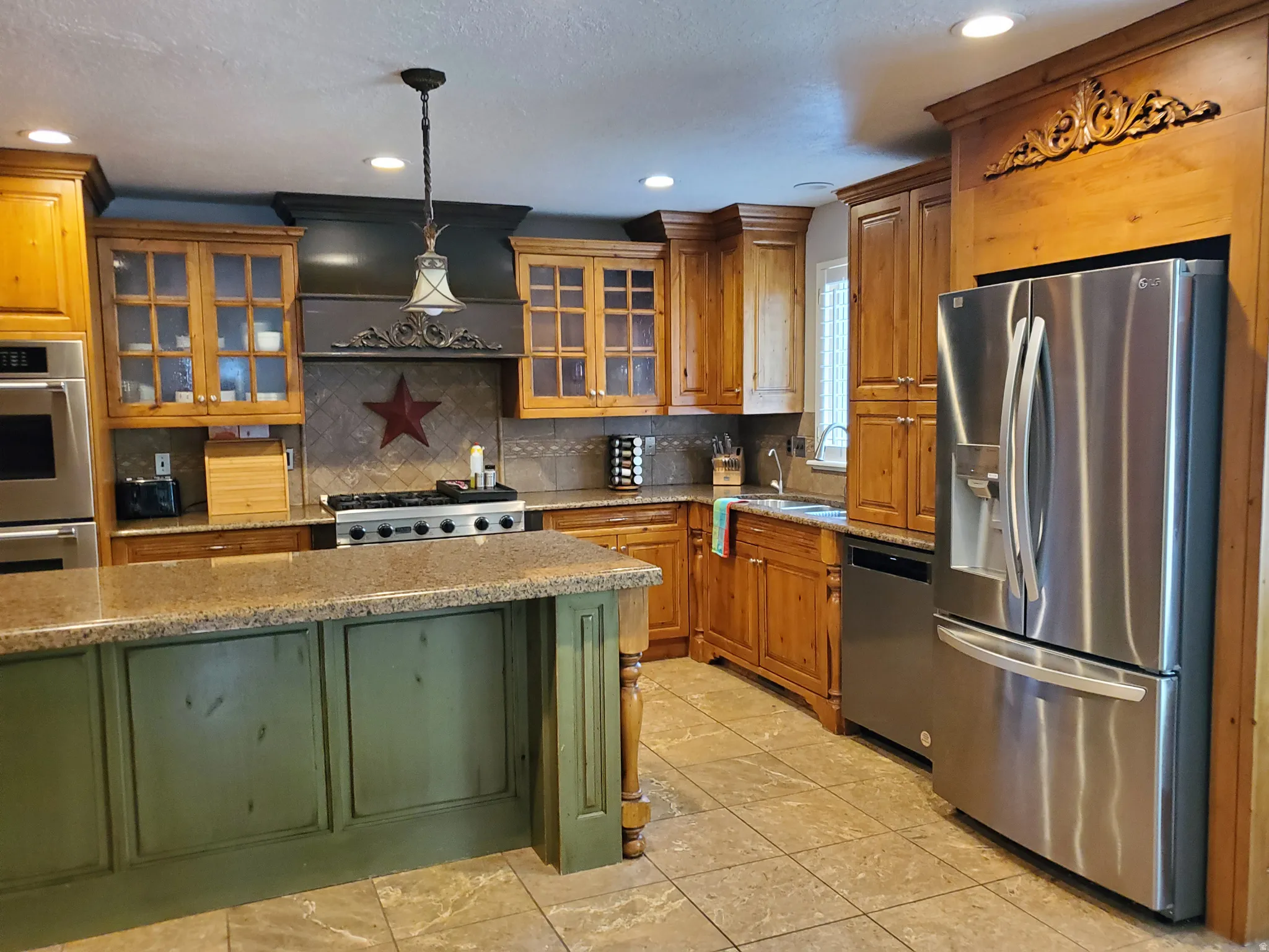 Kitchen featuring a central island with a distressed green finish, coordinating granite countertops, wood cabinetry with some glass-front doors, and stainless steel appliances