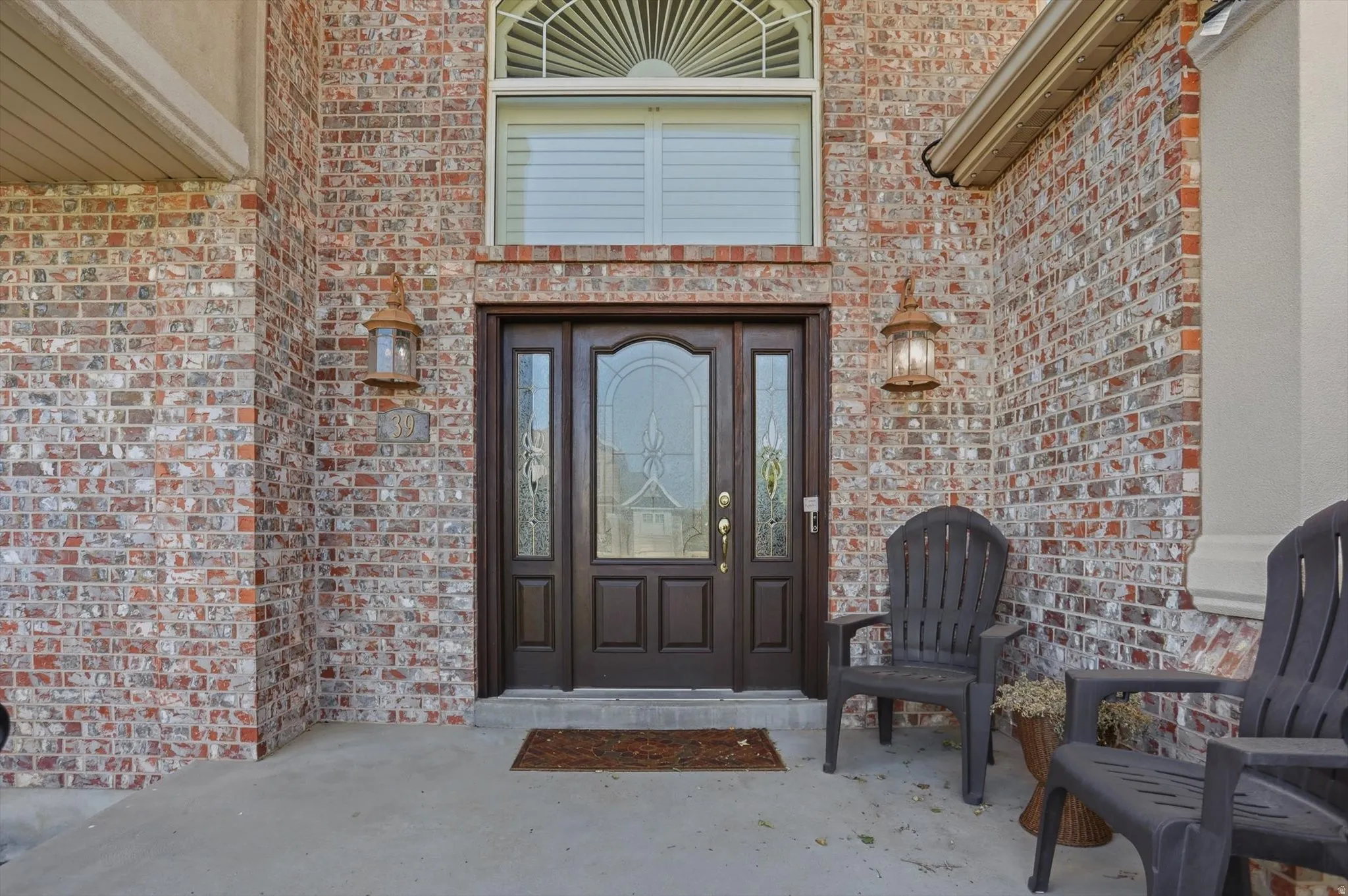 Brick exterior featuring a double entry door with decorative glass, transom window, and dual wall-mounted lanterns