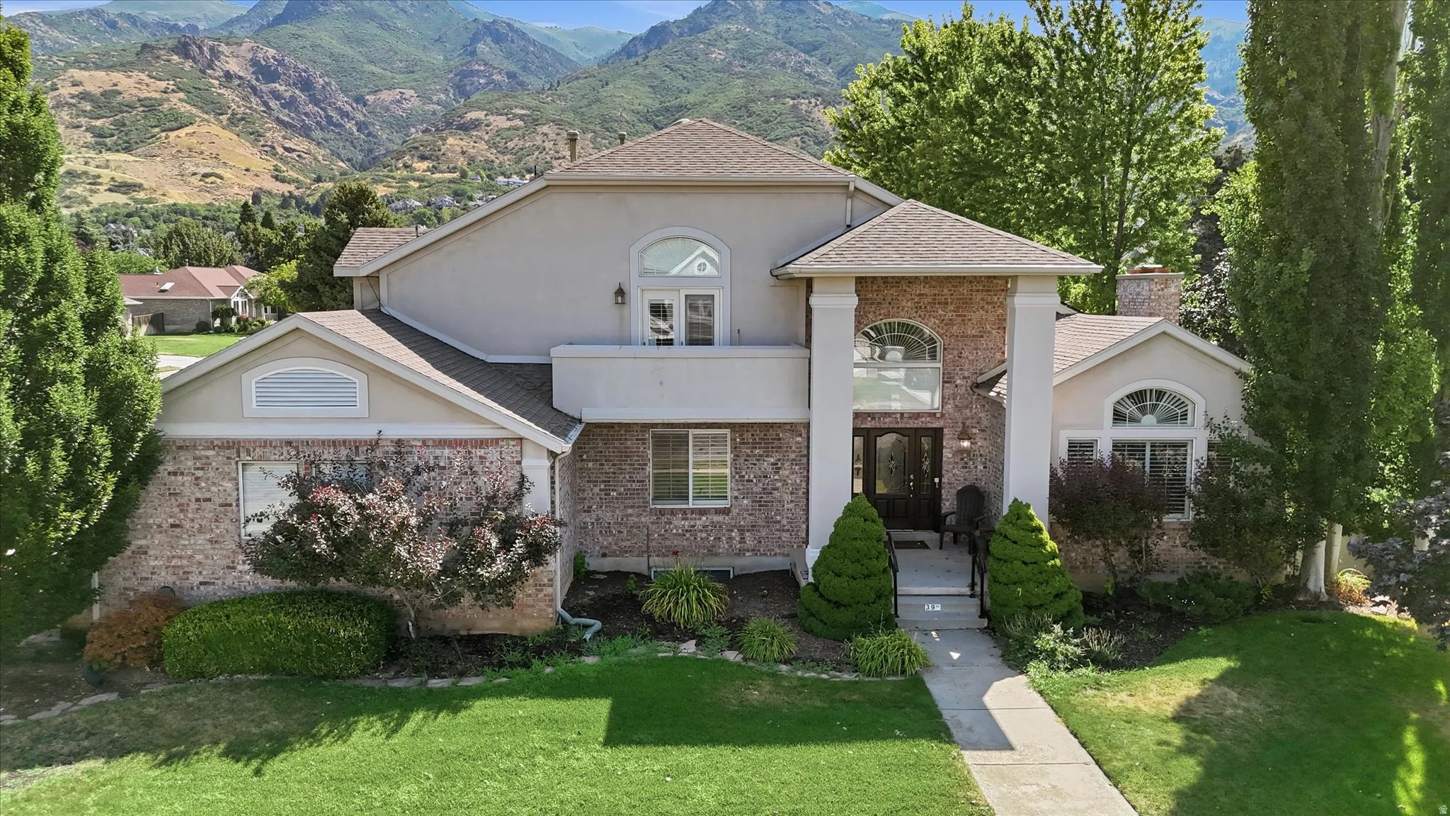 Stucco and brick exterior with arched windows, prominent entry columns, and a mountain backdrop