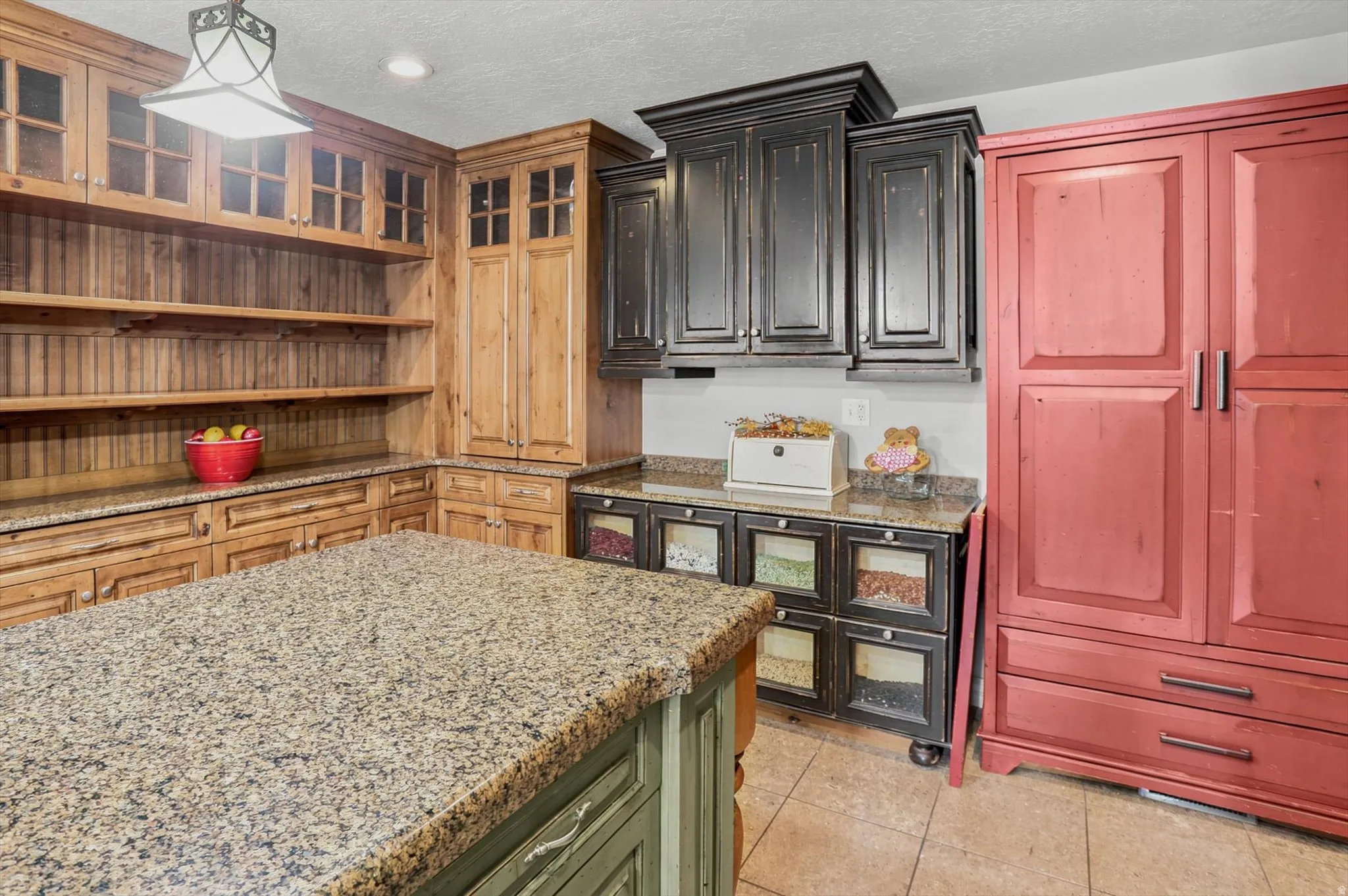Kitchen featuring a large island with a stone-finish countertop, custom wood cabinetry, open shelving, and tile flooring