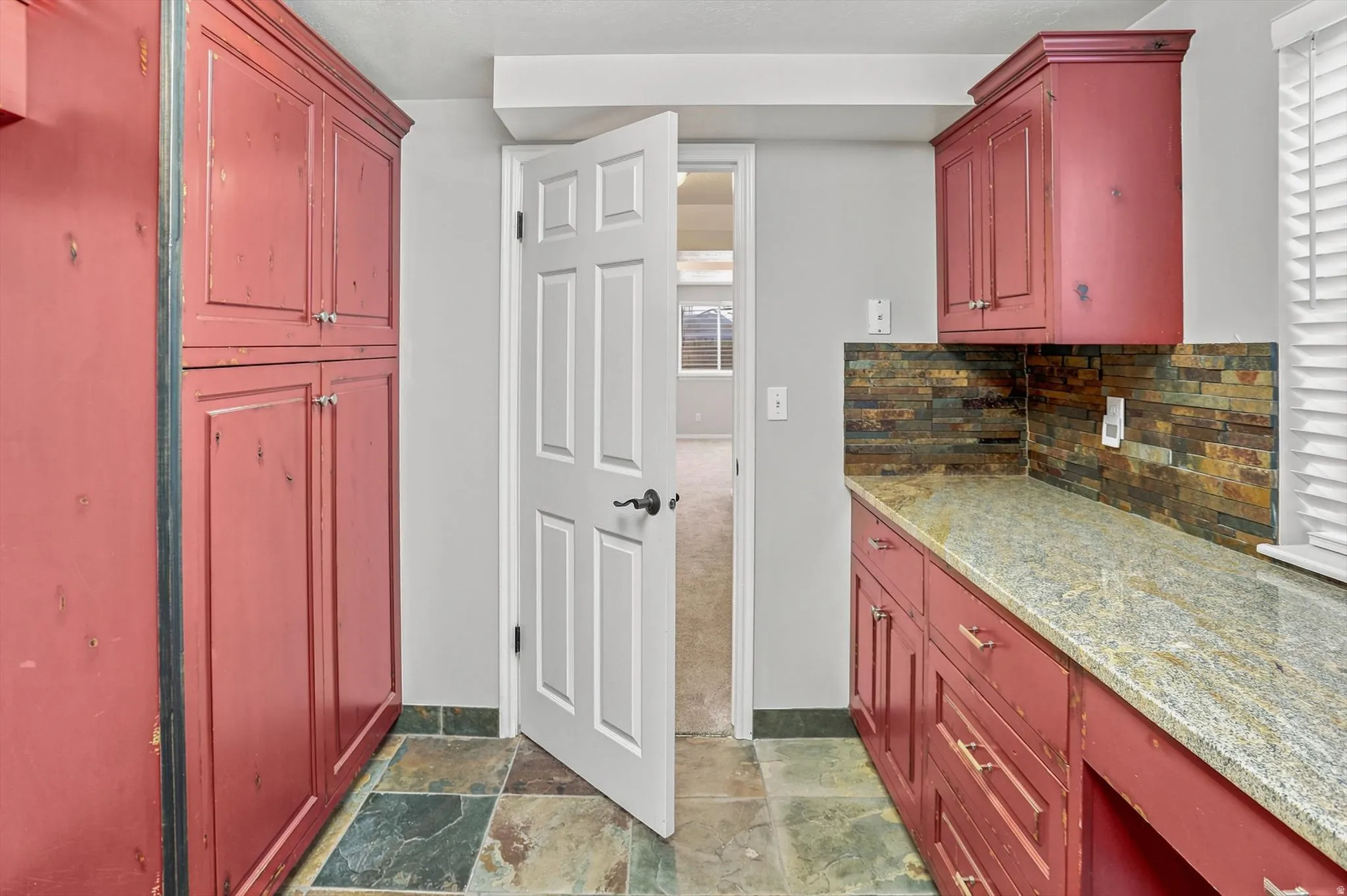 Utility space featuring red-painted cabinetry, a stone tile floor, and a stone veneer backsplash