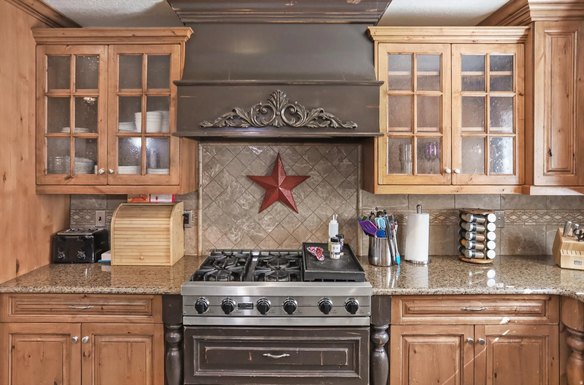 Professional-grade stainless steel range with a decorative range hood, complemented by natural wood cabinetry and granite countertops