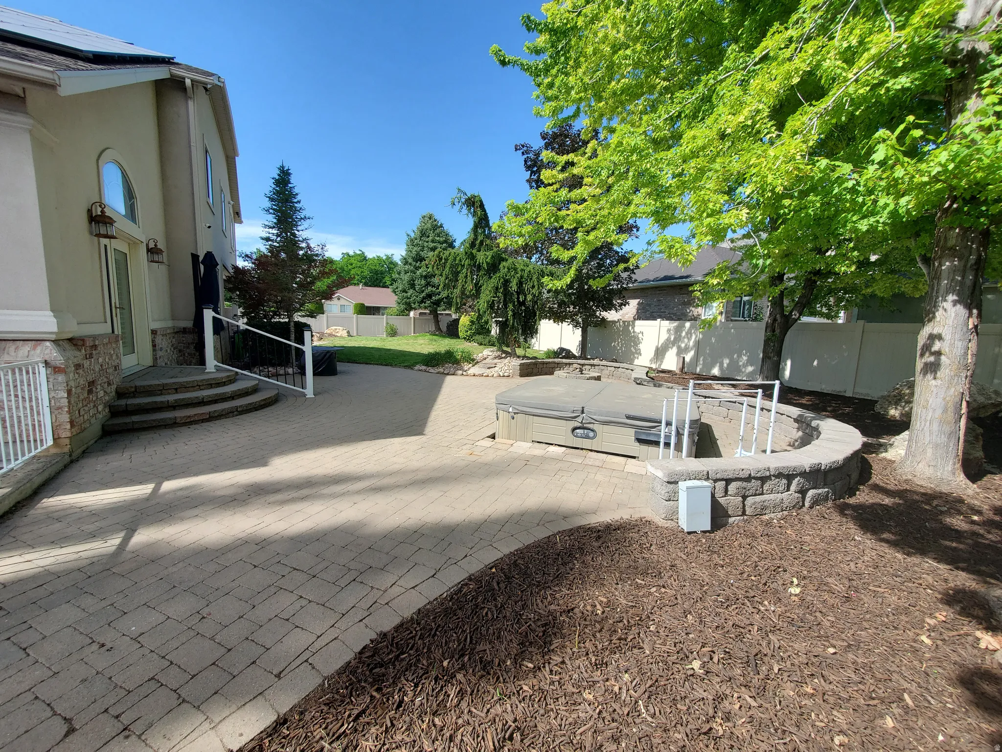 Expansive paver patio with a built-in hot tub, surrounded by a stone retaining wall