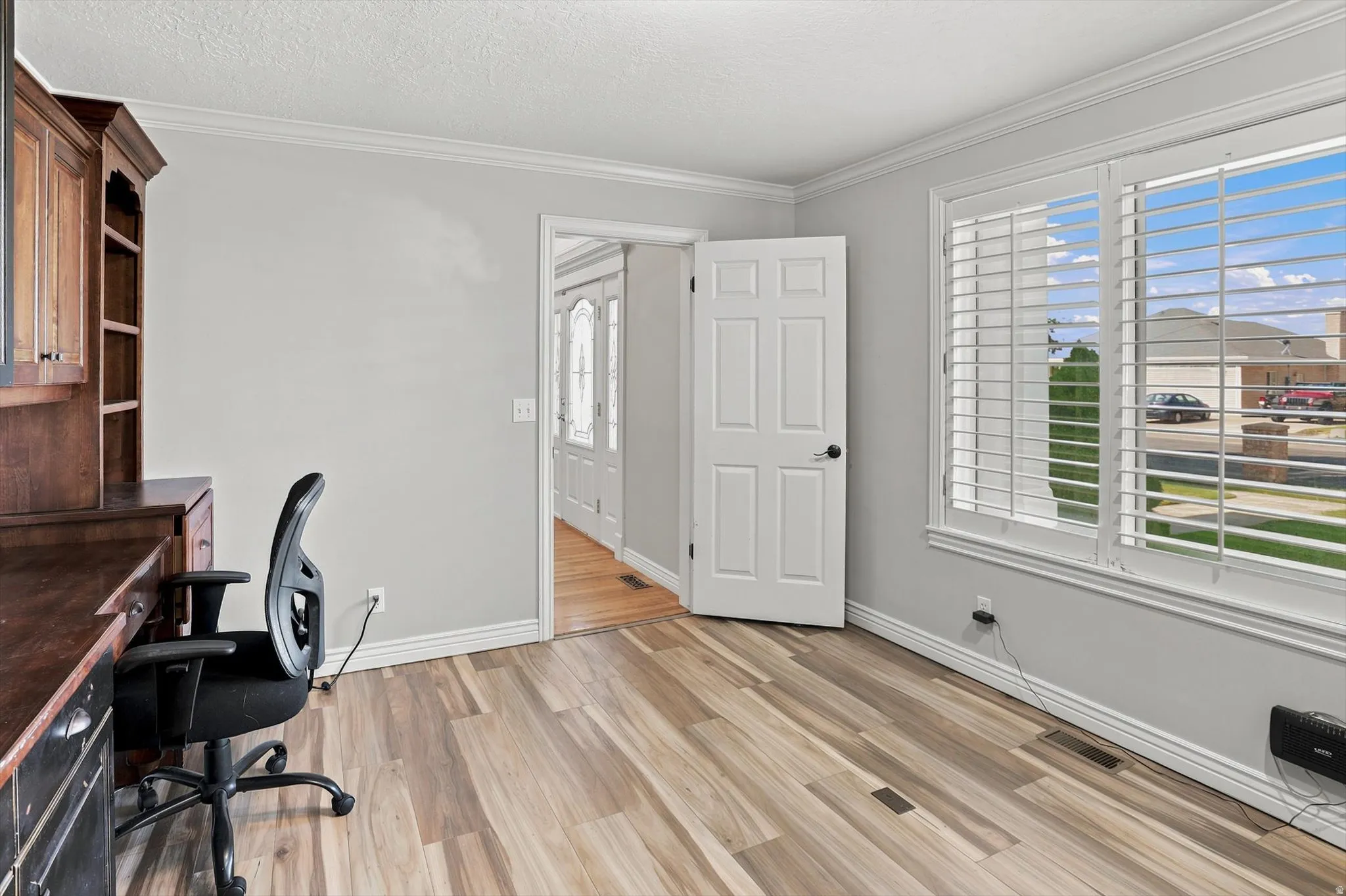 Spacious room featuring wood-finish flooring, light gray walls, and white crown molding