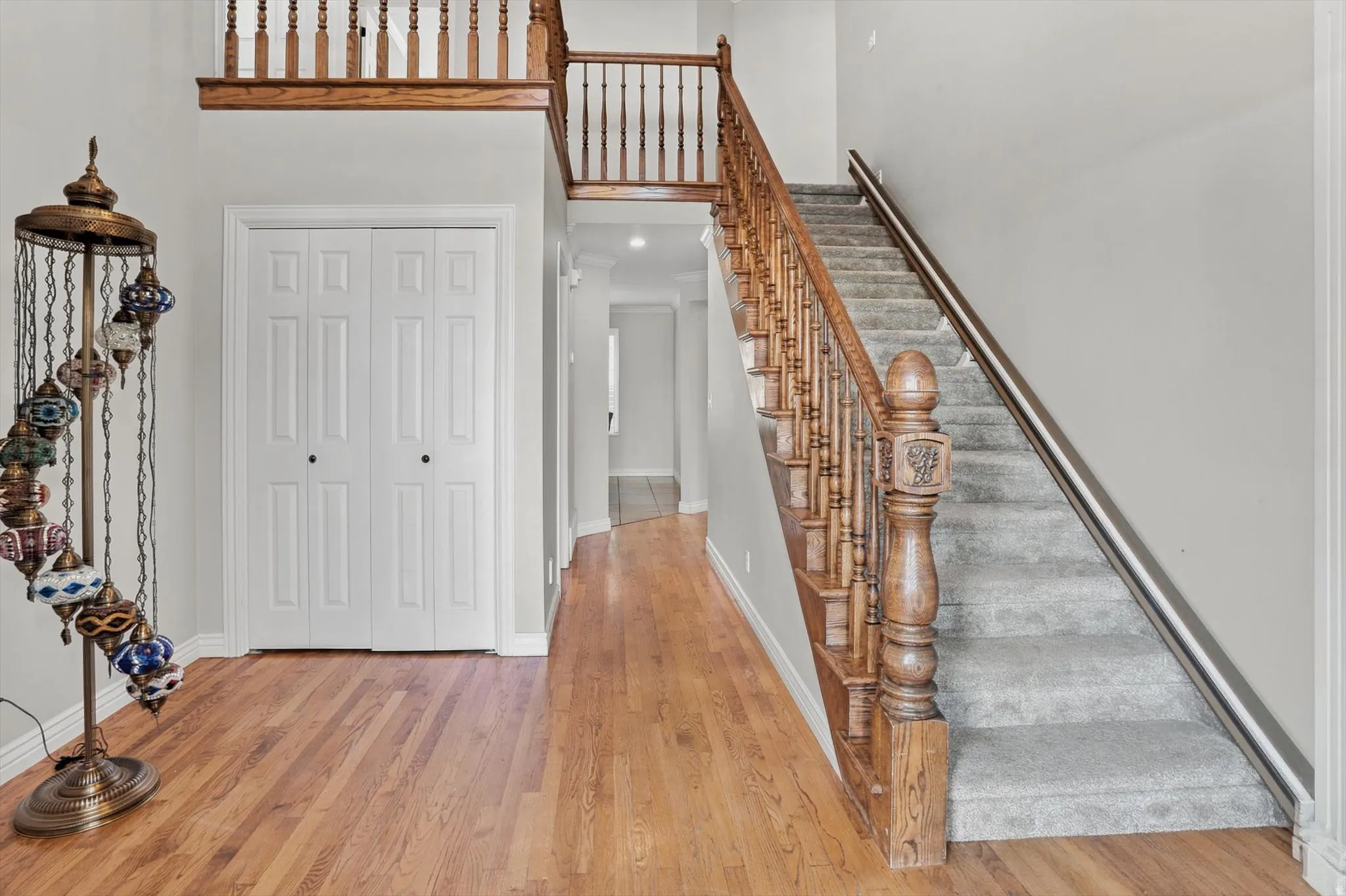 Hardwood flooring extending through the entry, featuring a carpeted staircase with a wood balustrade