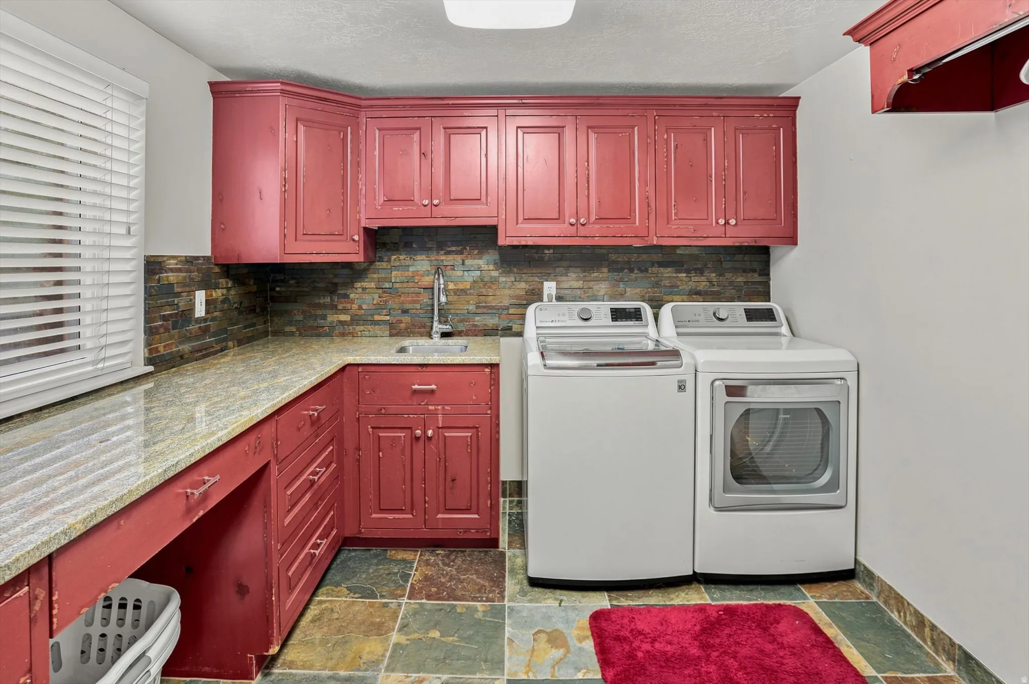 Utility room featuring red cabinetry, a granite-look countertop, and a stacked stone-look backsplash