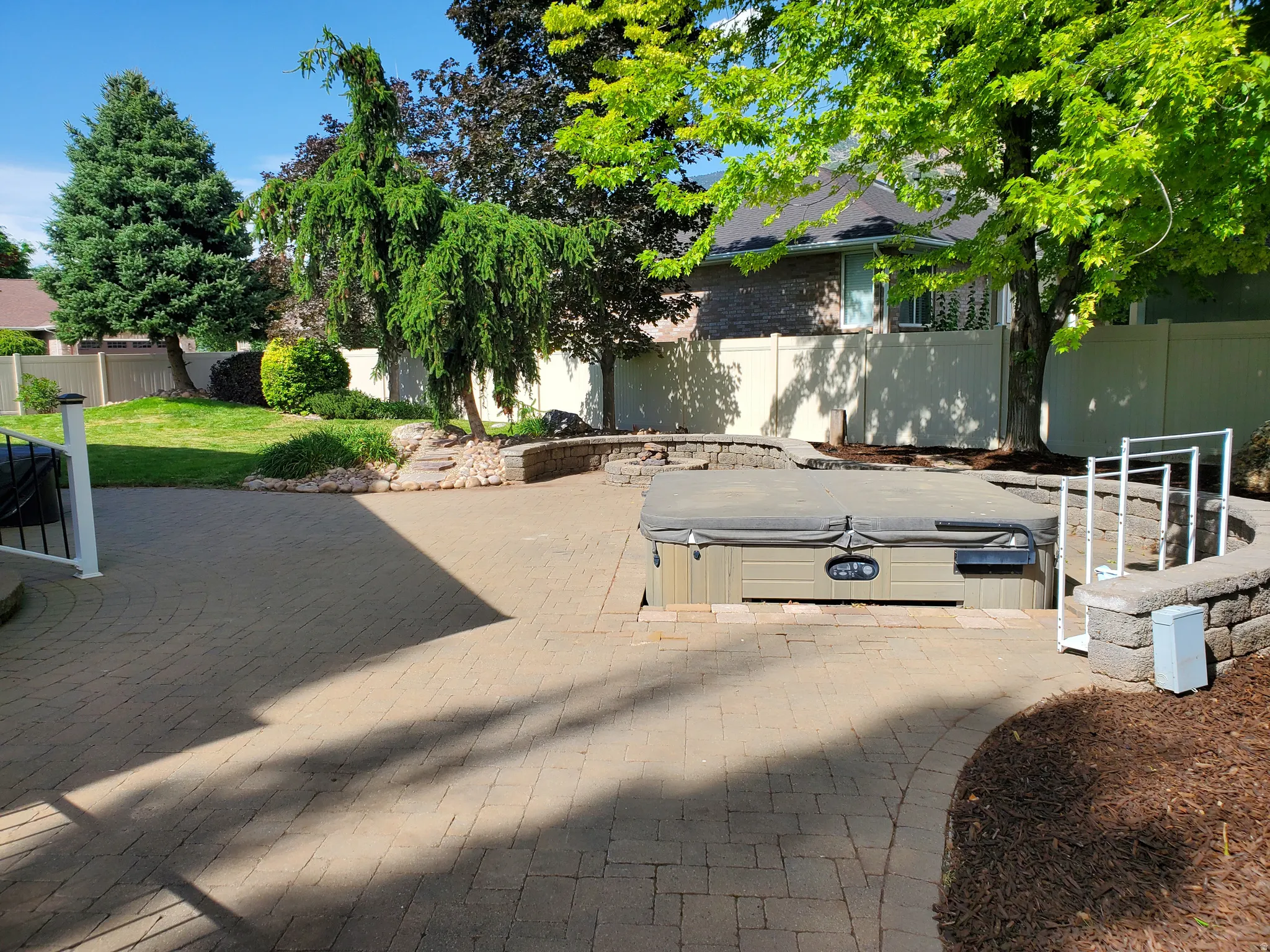 Expansive brick paver patio featuring a built-in spa, surrounding stone retaining walls, and mature landscaping