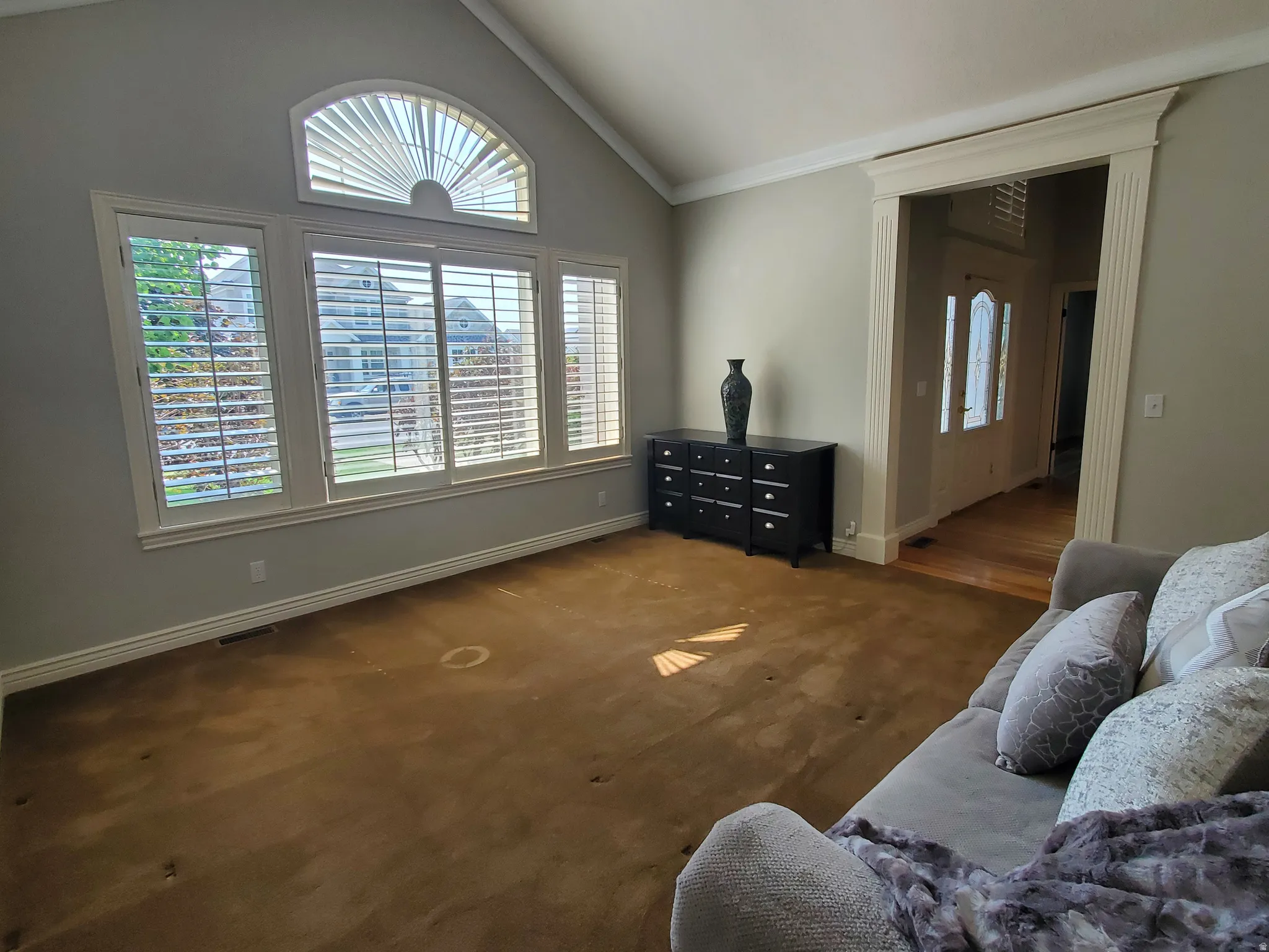 Spacious living area featuring vaulted ceilings, crown molding, and extensive window treatments including an arched transom window