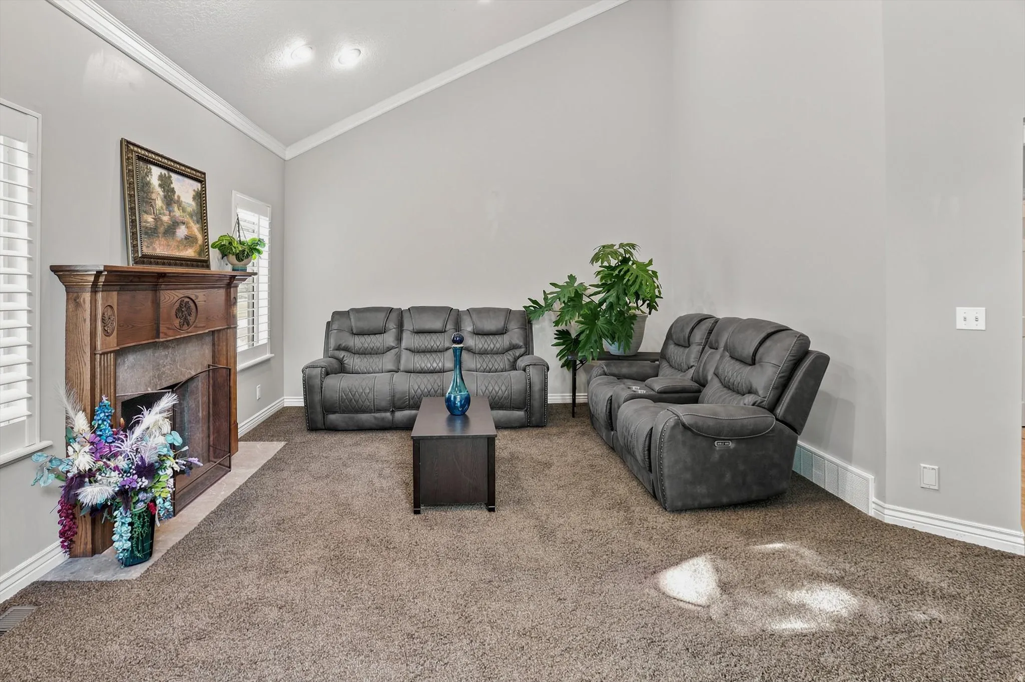 Vaulted ceiling living area featuring a decorative wood mantel and surround fireplace, plantation-style window shutters, and neutral-toned wall paint