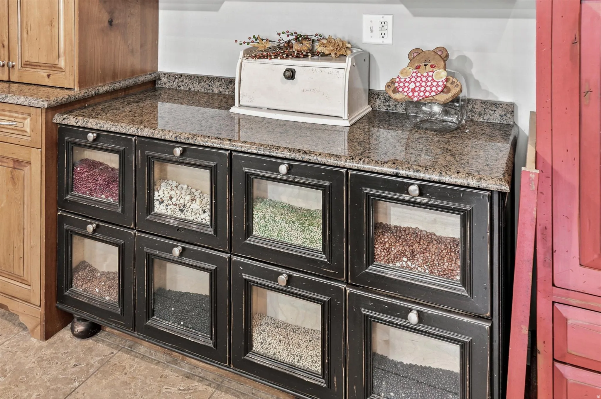 Distressed black cabinetry featuring clear-paneled drawers and circular pulls, topped with a speckled granite countertop