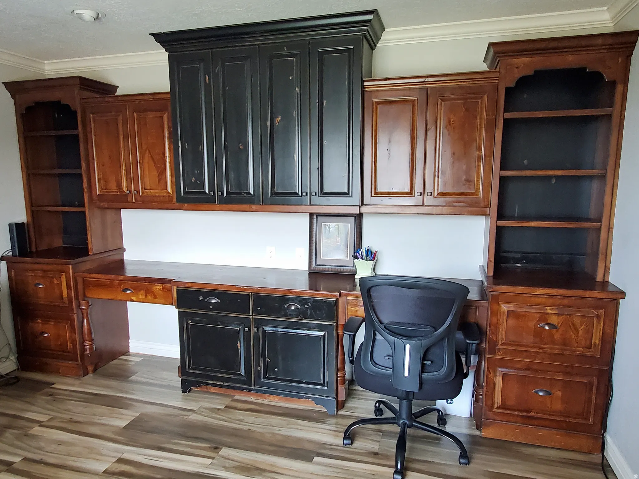 Built-in desk unit featuring wood-finish flooring, recessed lighting, crown molding, and a combination of natural wood and distressed black cabinetry