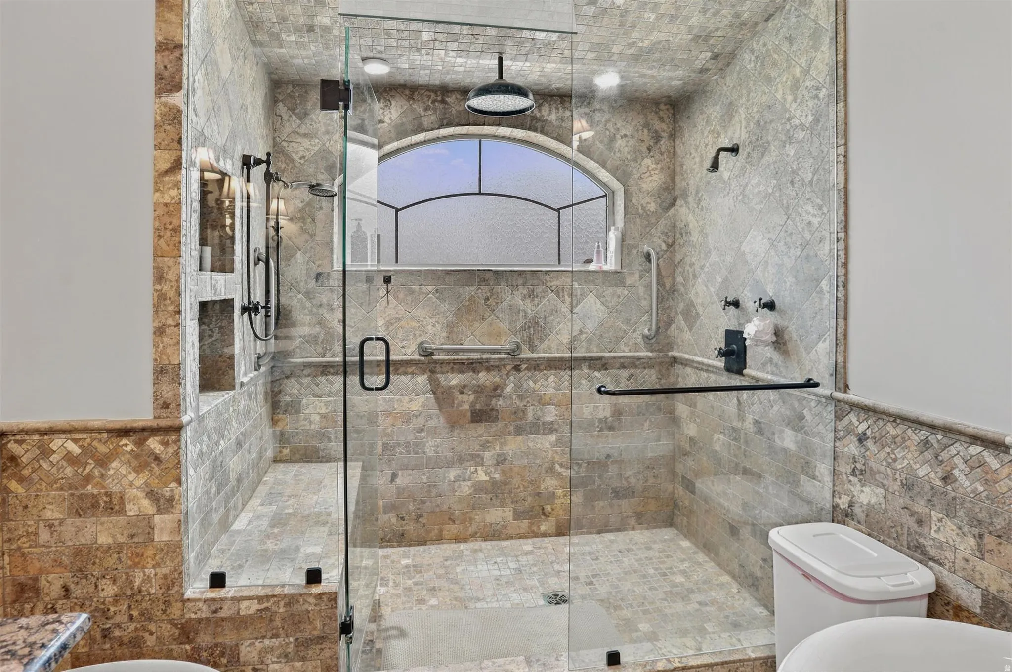 Glass-enclosed shower with full tile surround and floor, featuring a built-in bench, two recessed niches, and an arched transom window
