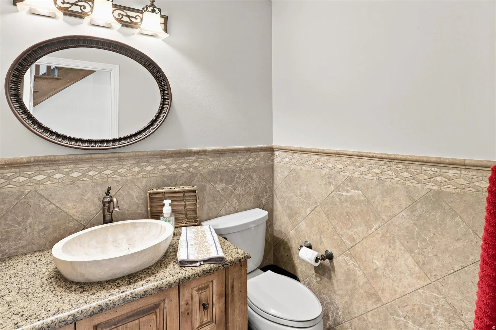 Powder room featuring a vessel sink, stone countertop, wood-finish vanity, decorative wall tiling, and an ornate mirror with overhead lighting