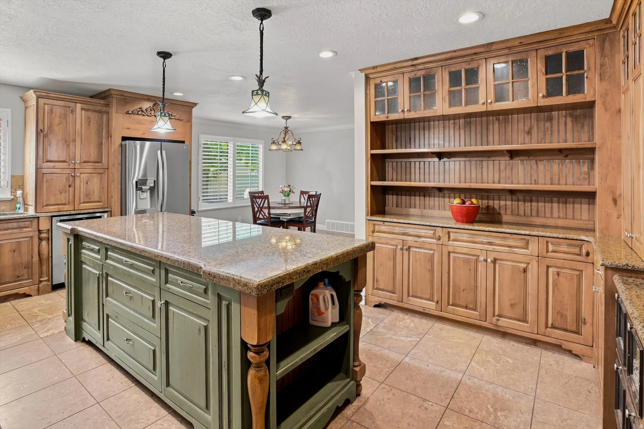 Kitchen featuring a large central island with a granite-style countertop, a built-in stainless steel refrigerator, extensive wood cabinetry, and tile flooring