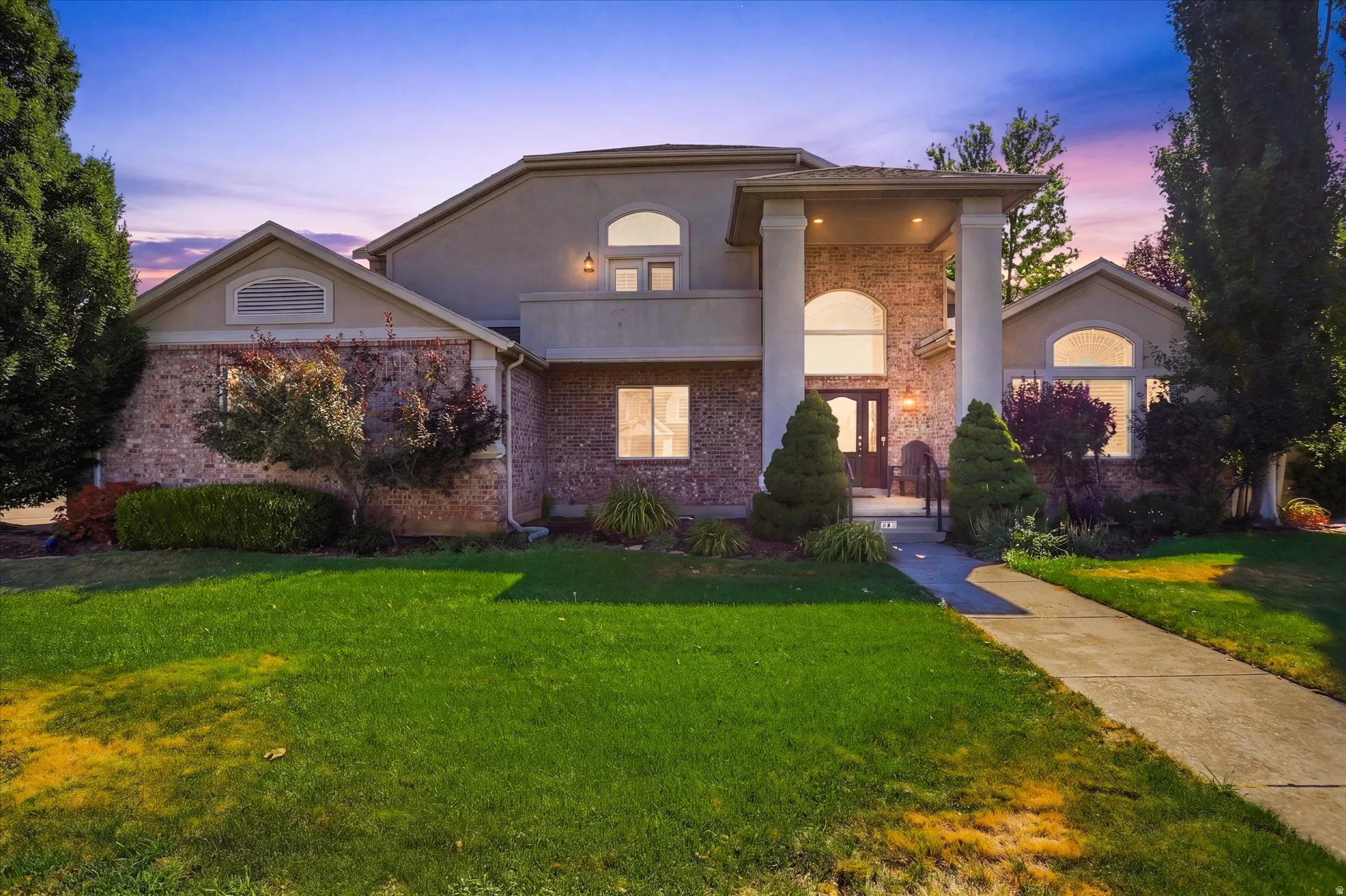 Stately stucco and brick exterior featuring a prominent covered entryway with large columns, arched windows, and a concrete pathway
