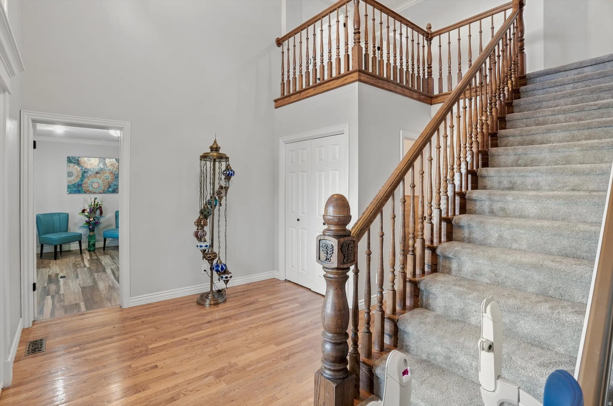 Foyer featuring hardwood flooring, a carpeted staircase with wood banister and balusters, a built-in coat closet, and a high ceiling