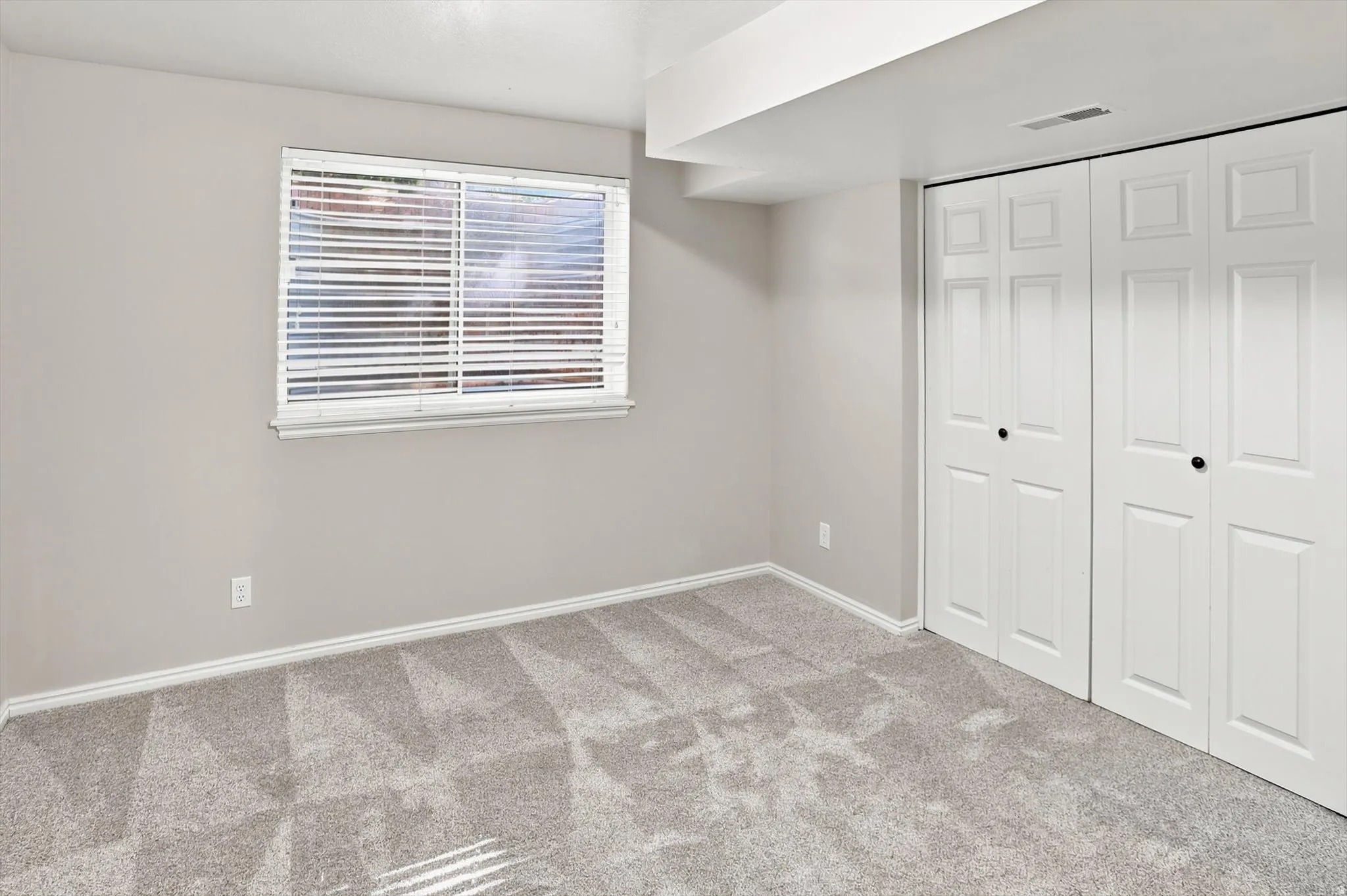 Bedroom featuring light gray walls, patterned gray carpeting, white baseboards, and a white window with horizontal blinds