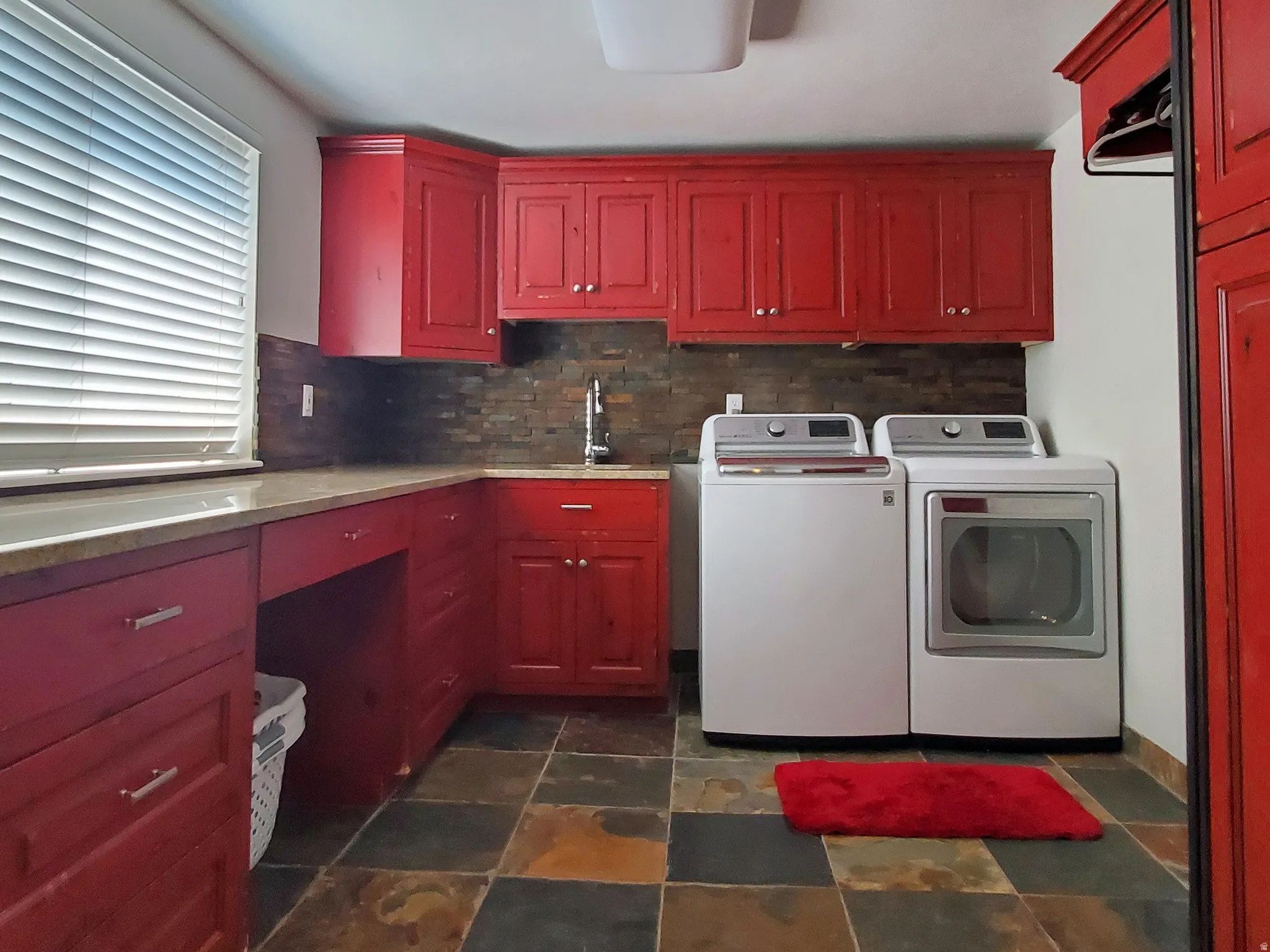 Laundry room featuring extensive red cabinetry, a granite-finish countertop, and a dark stone-finish backsplash