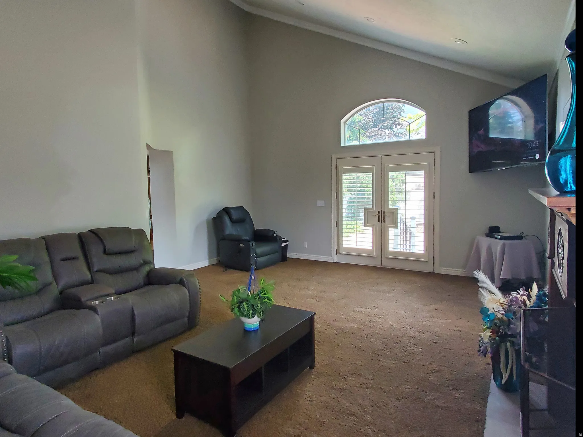 Vaulted ceiling living area featuring double French doors with interior plantation shutters and an arched transom window
