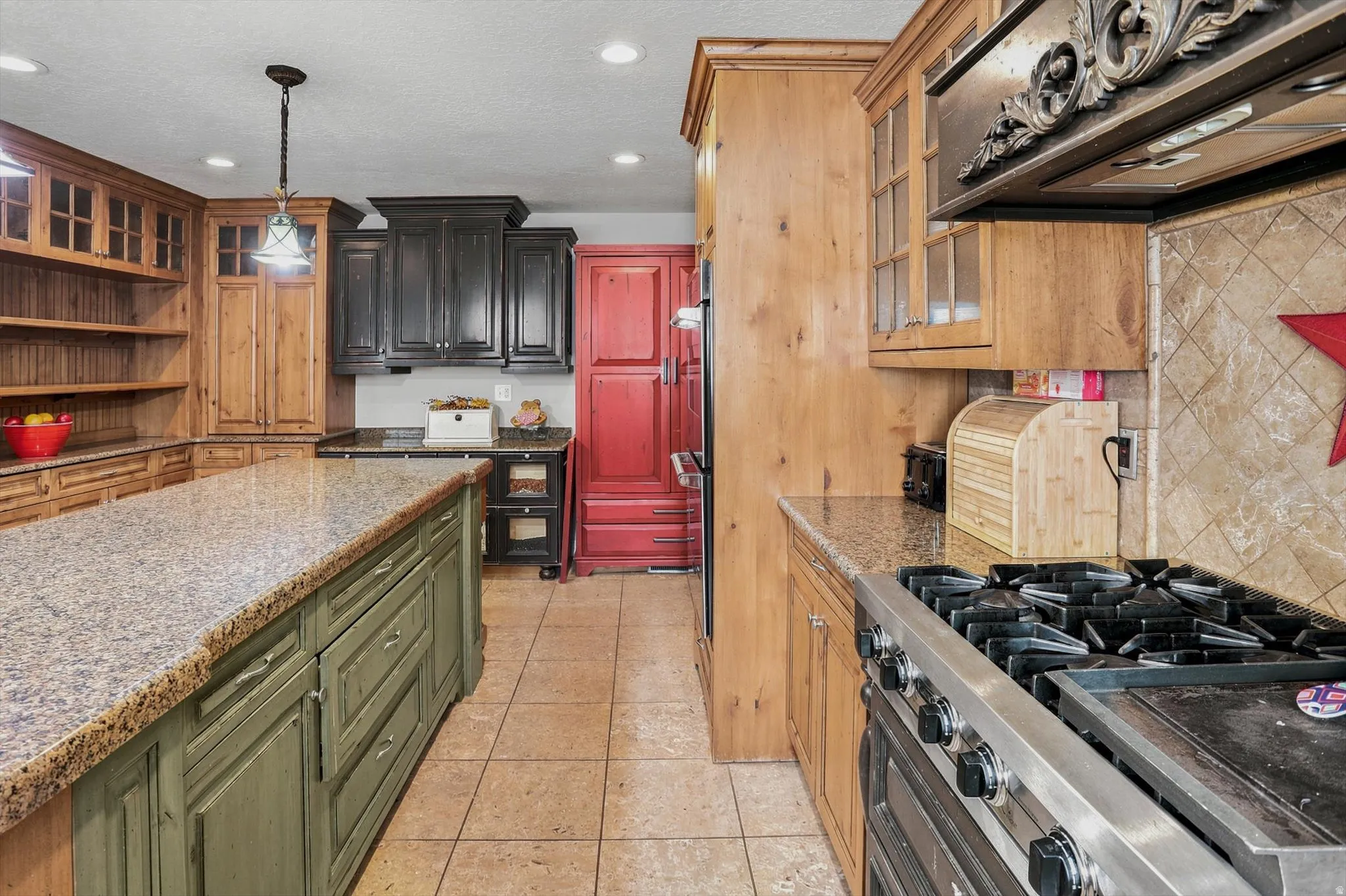 Spacious kitchen featuring an expansive granite-top island with integrated cabinetry, tile flooring, diverse cabinetry finishes, a built-in range, and a tiled backsplash