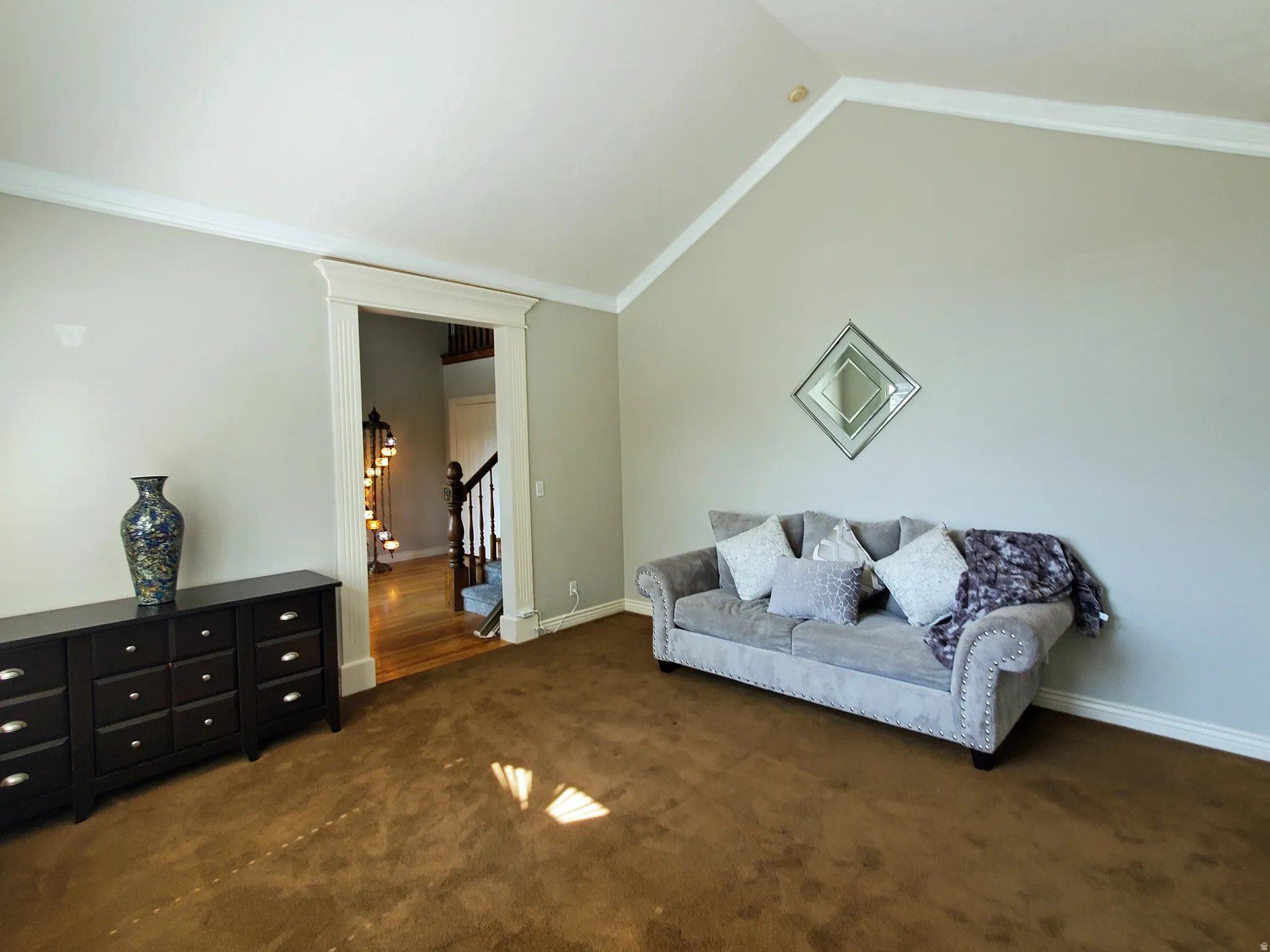 Spacious room featuring vaulted ceilings, crown molding, and a wide doorway with detailed trim leading to a staircase with wood railings and treads