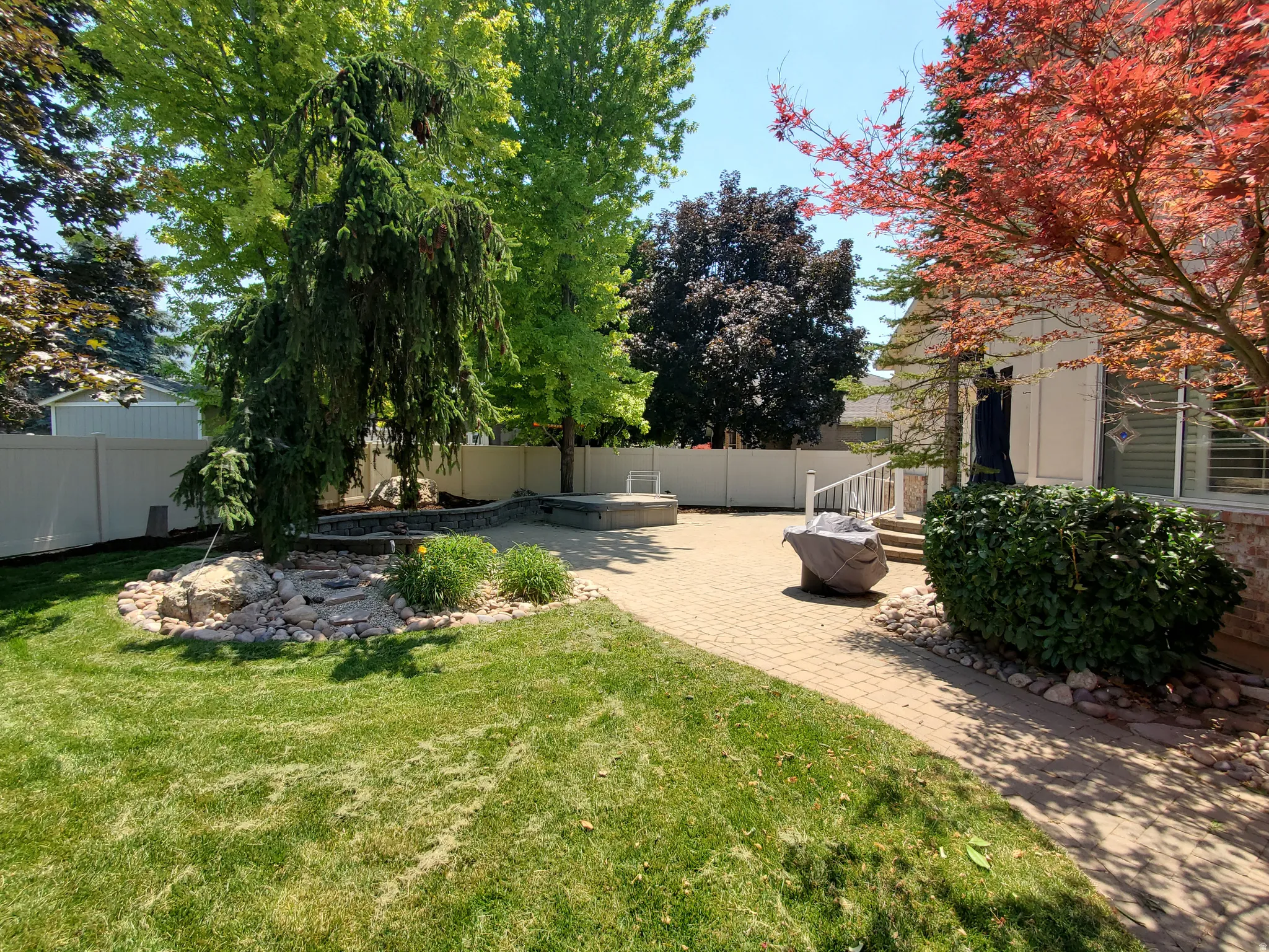 Backyard featuring a paved patio area, green lawn, and a light-colored privacy fence