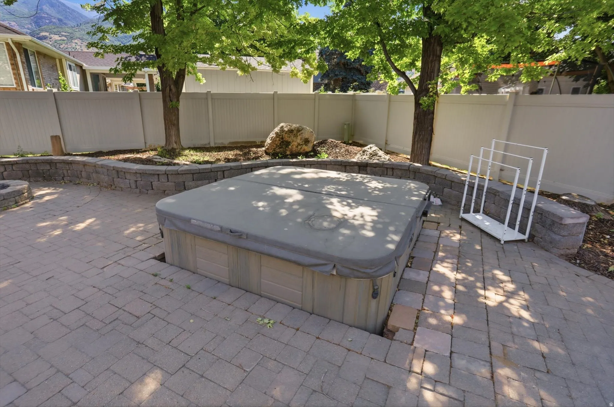 Outdoor spa area featuring a built-in spa, paver patio, stone retaining wall, mature trees, and privacy fencing