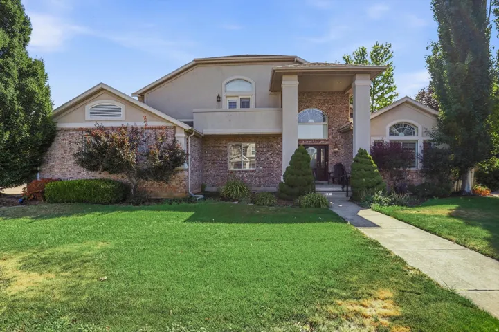 Brick and stucco contemporary home featuring a welcoming front facade with arched entryway, multi-level design with rounded turret elements, manicured lawn with mature landscaping including evergreen plantings, concrete walkway leading to the entrance, an