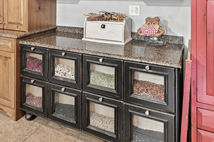 Distressed black cabinetry featuring clear-paneled drawers and circular pulls, topped with a speckled granite countertop