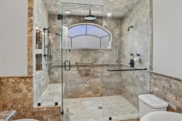 Glass-enclosed shower with full tile surround and floor, featuring a built-in bench, two recessed niches, and an arched transom window