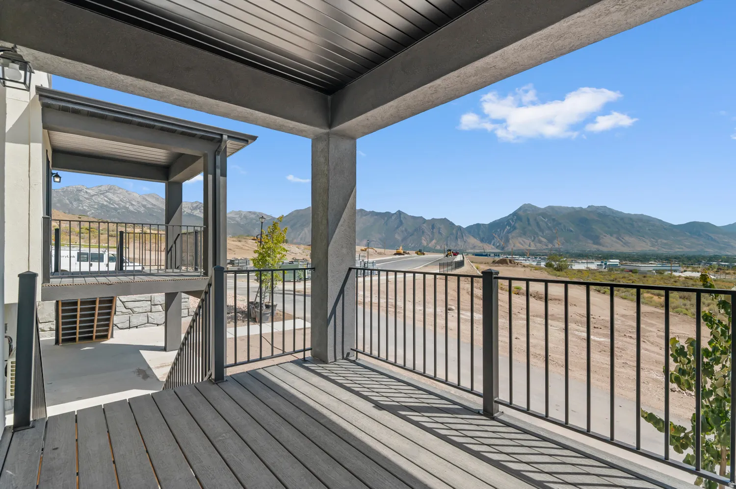 Upper-level outdoor deck featuring mountain scenery, composite decking, black metal railings, and a covered ceiling