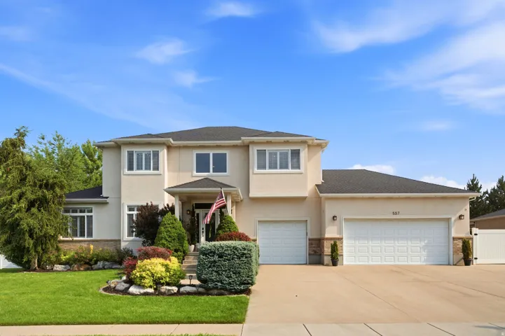Stucco exterior residence featuring a covered entry, established landscaping, dual garage doors, and a concrete driveway