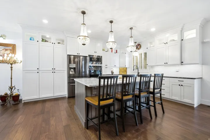 Bright kitchen featuring white shaker cabinetry, stainless steel appliances, a large center island with seating, pendant lighting, and wood-finish flooring