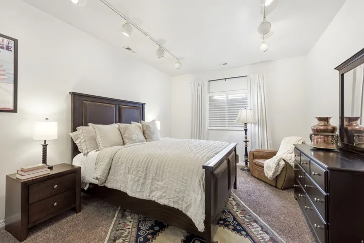 Spacious room featuring white walls, track lighting, and a window with blinds and curtains