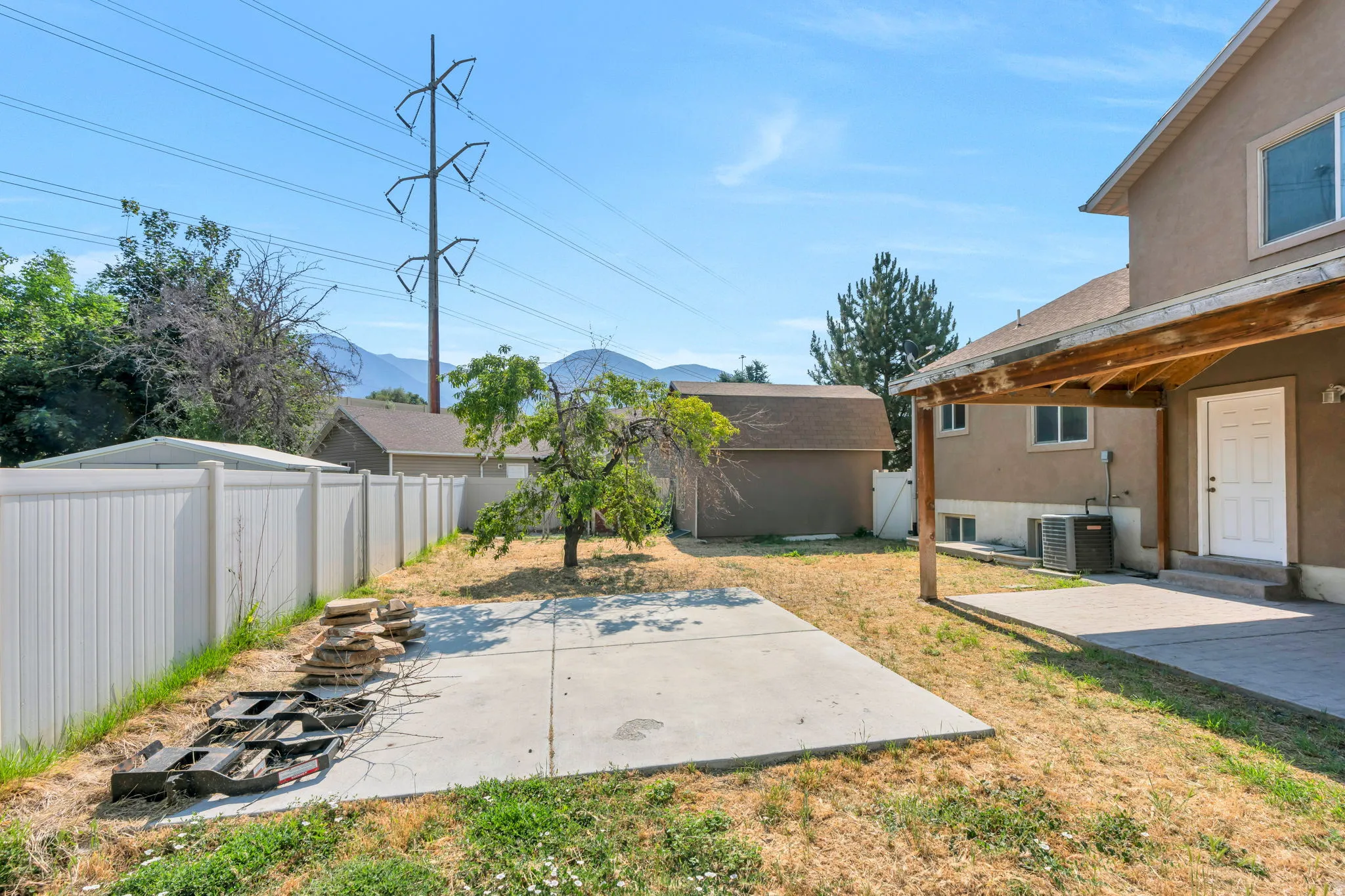 Rear exterior with stucco siding, covered patio, white vinyl fencing, and a separate storage shed