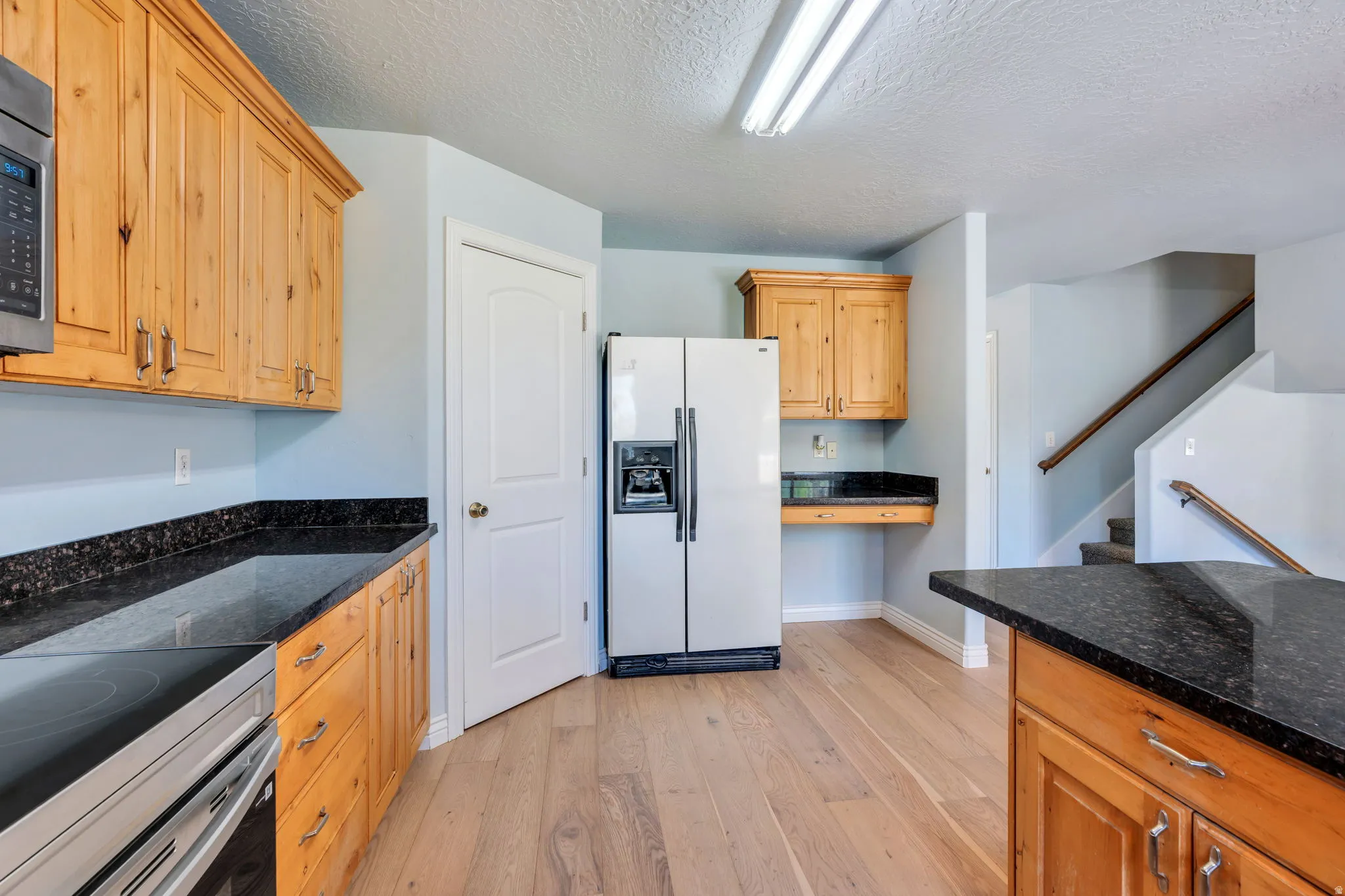 Kitchen featuring wood cabinetry, dark granite countertops, wood-finish flooring, and stainless steel appliances