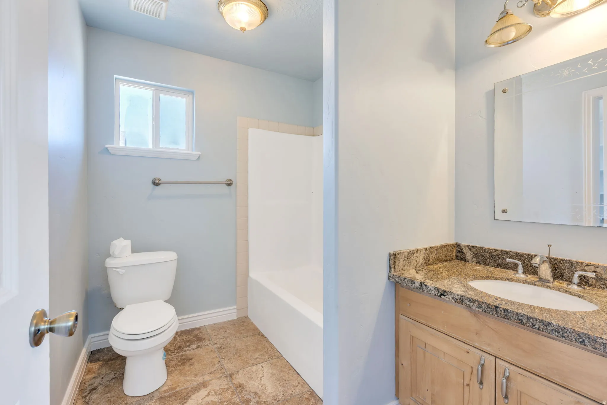 Bathroom featuring a light wood-finish vanity with granite countertop, an integrated sink, and a framed mirror